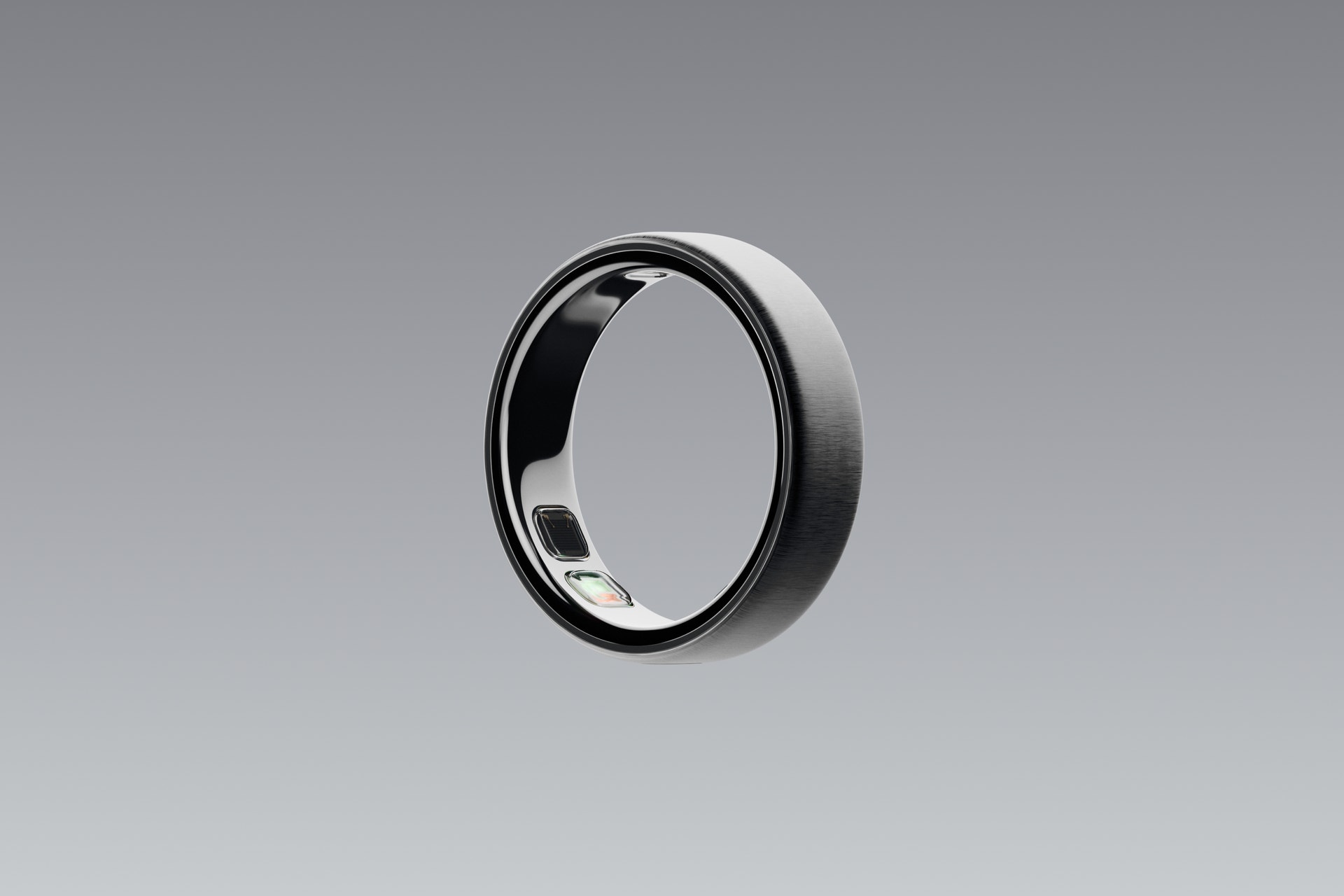 Oura Ring 5 i borstad silver, en smart ring med svart och silver design, fotograferad mot grå bakgrund.