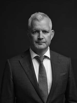 Porträttfoto av en man i kostym och slips mot mörk bakgrund