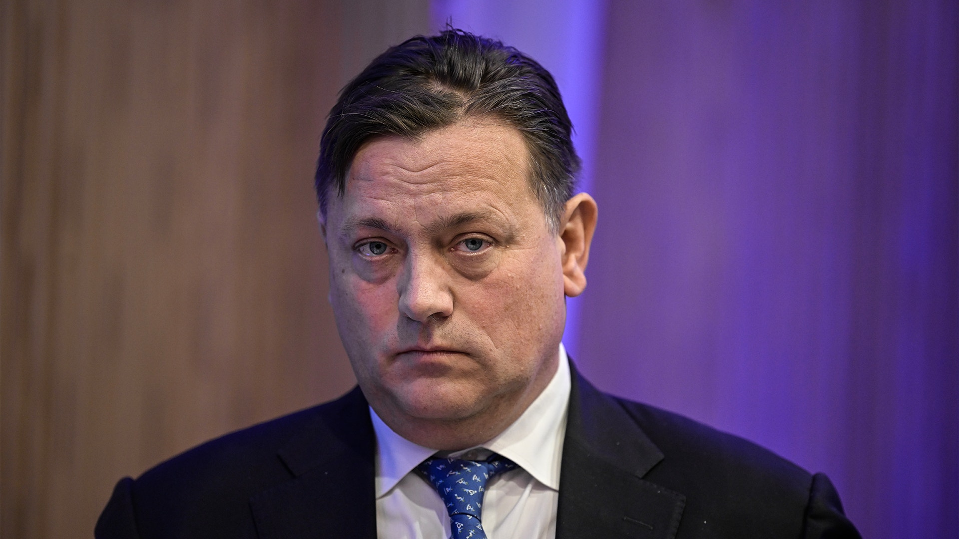 Porträtt av en man i kostym och slips mot en lila belyst bakgrund