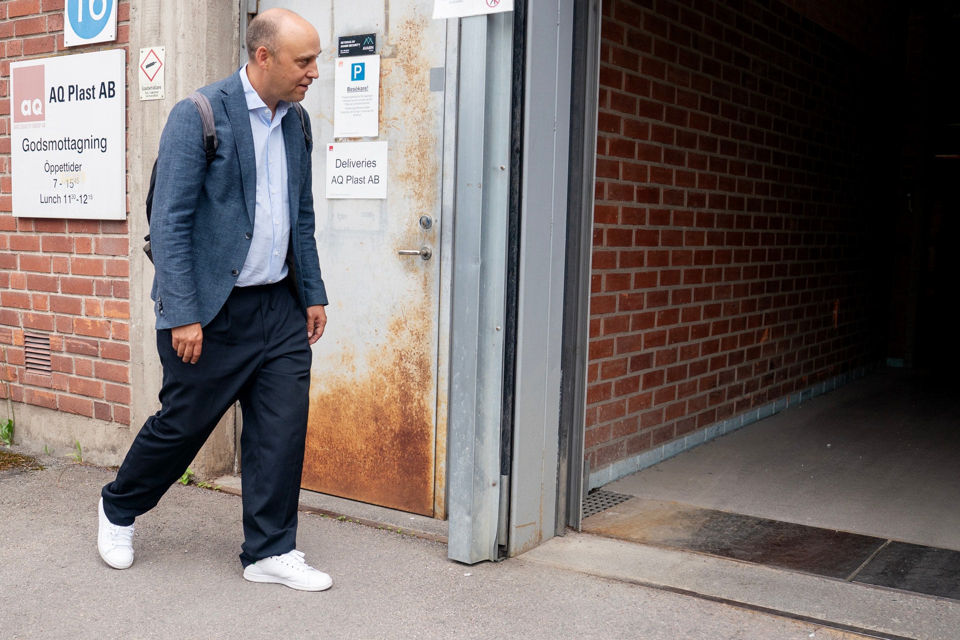 Man i blå kavaj och vita skor står utanför en tegelbyggnad
