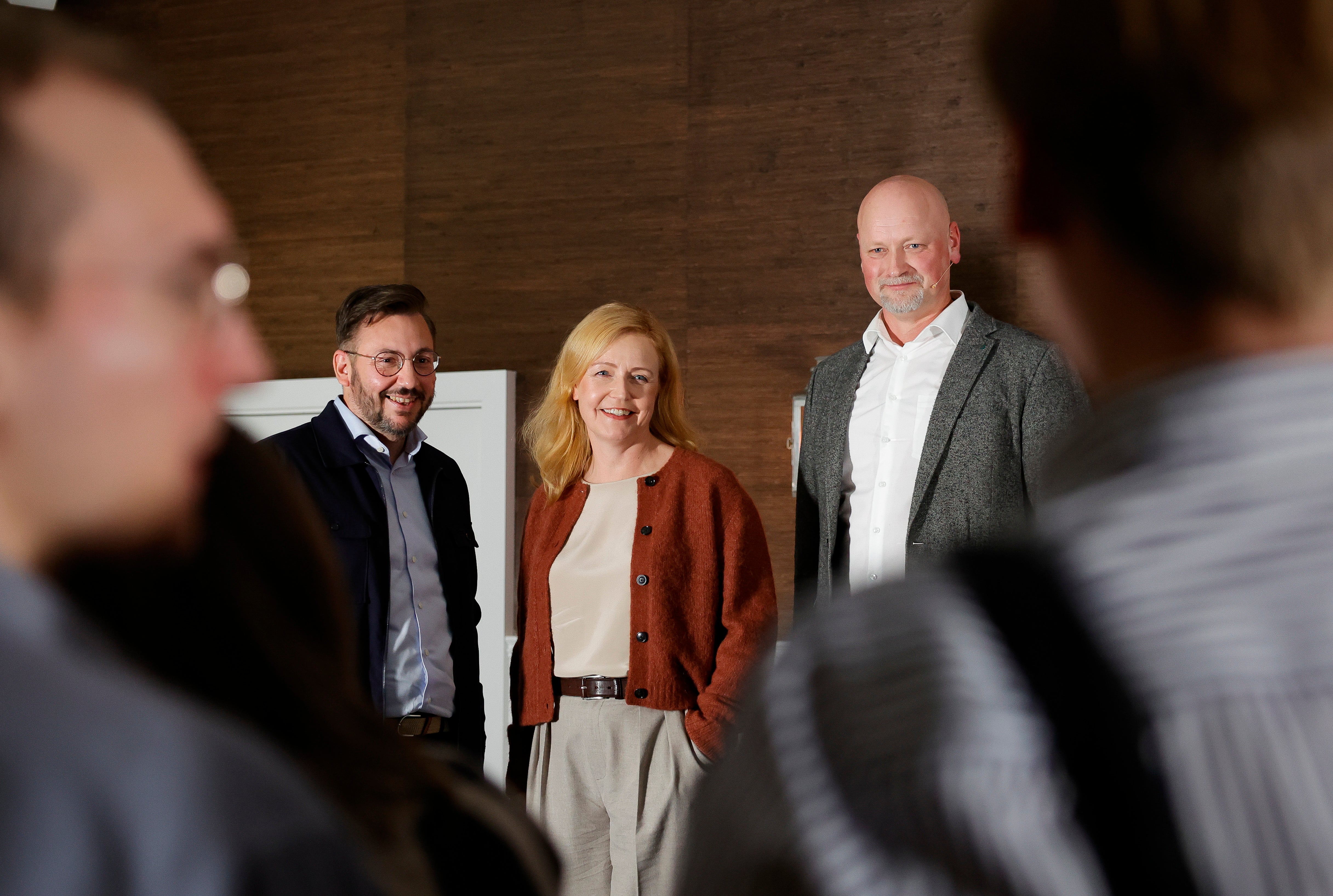 Tre personer i affärskläder står tillsammans på en gata framför gamla byggnader.