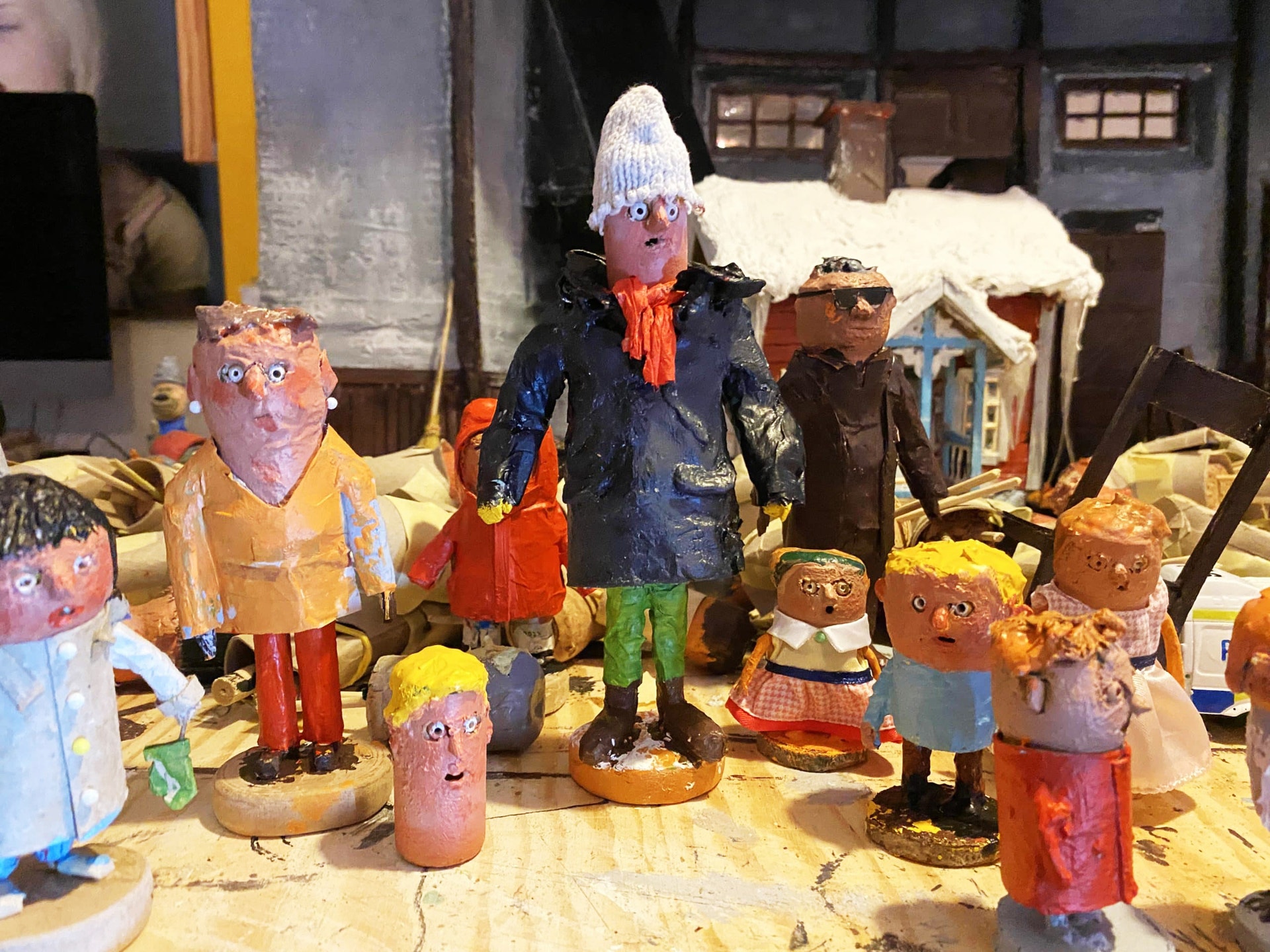 Samling av handgjorda träfigurer i olika färger och storlekar utställda på ett bord. Figurerna föreställer människor med olika kläder och accessoarer.