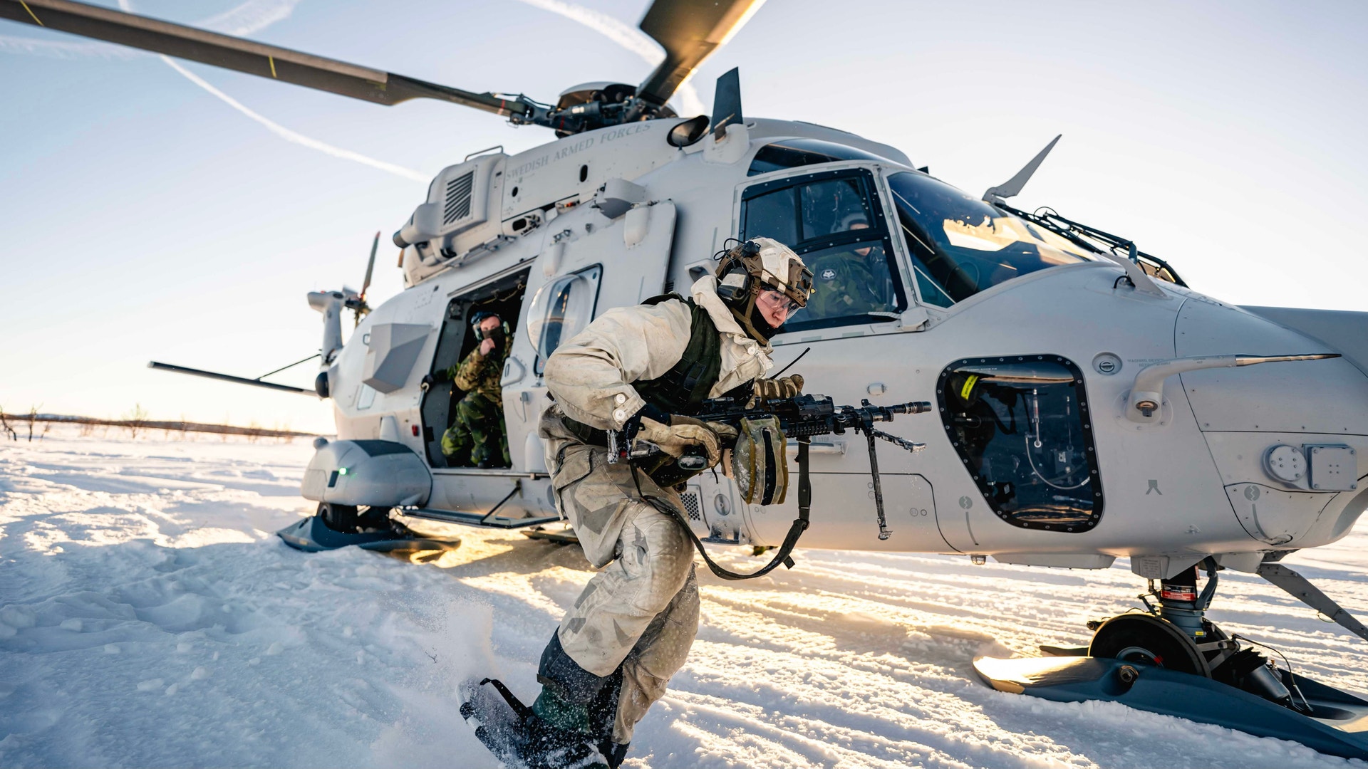 Militär helikopter på snöig mark med beväpnad personal som går ut från helikoptern.