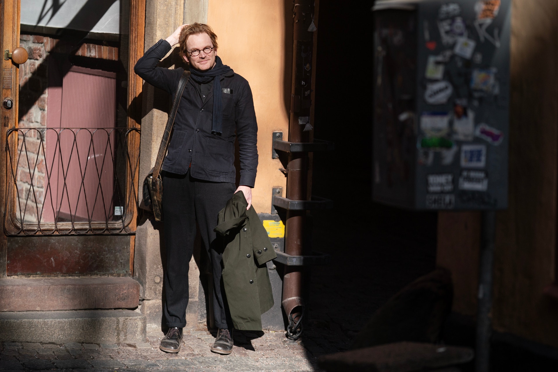 En person i svart jacka och glasögon står i en smal gata med gula väggar.
