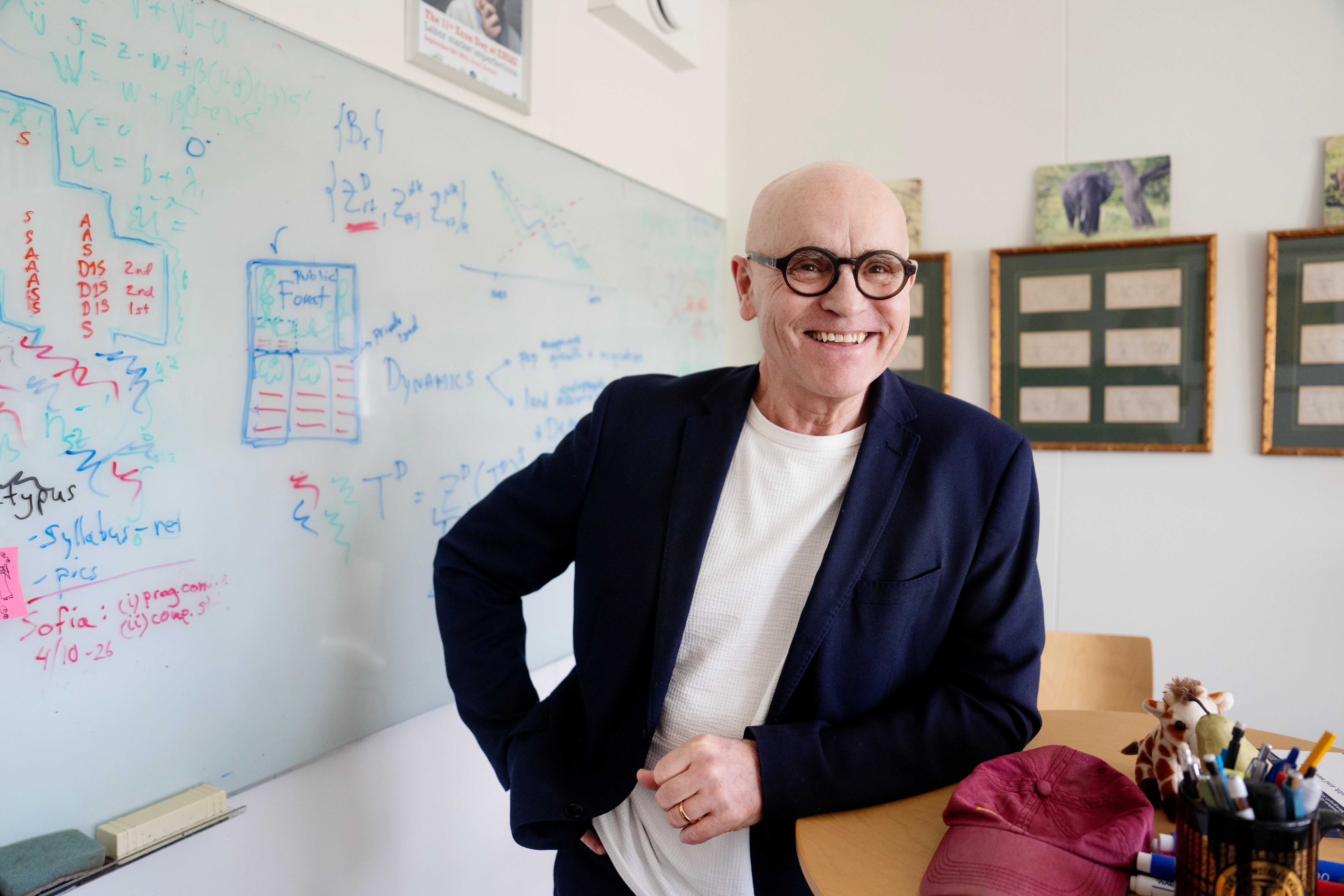 Man i glasögon och mörk kavaj poserar i ett arbetsrum med whiteboard i bakgrunden.