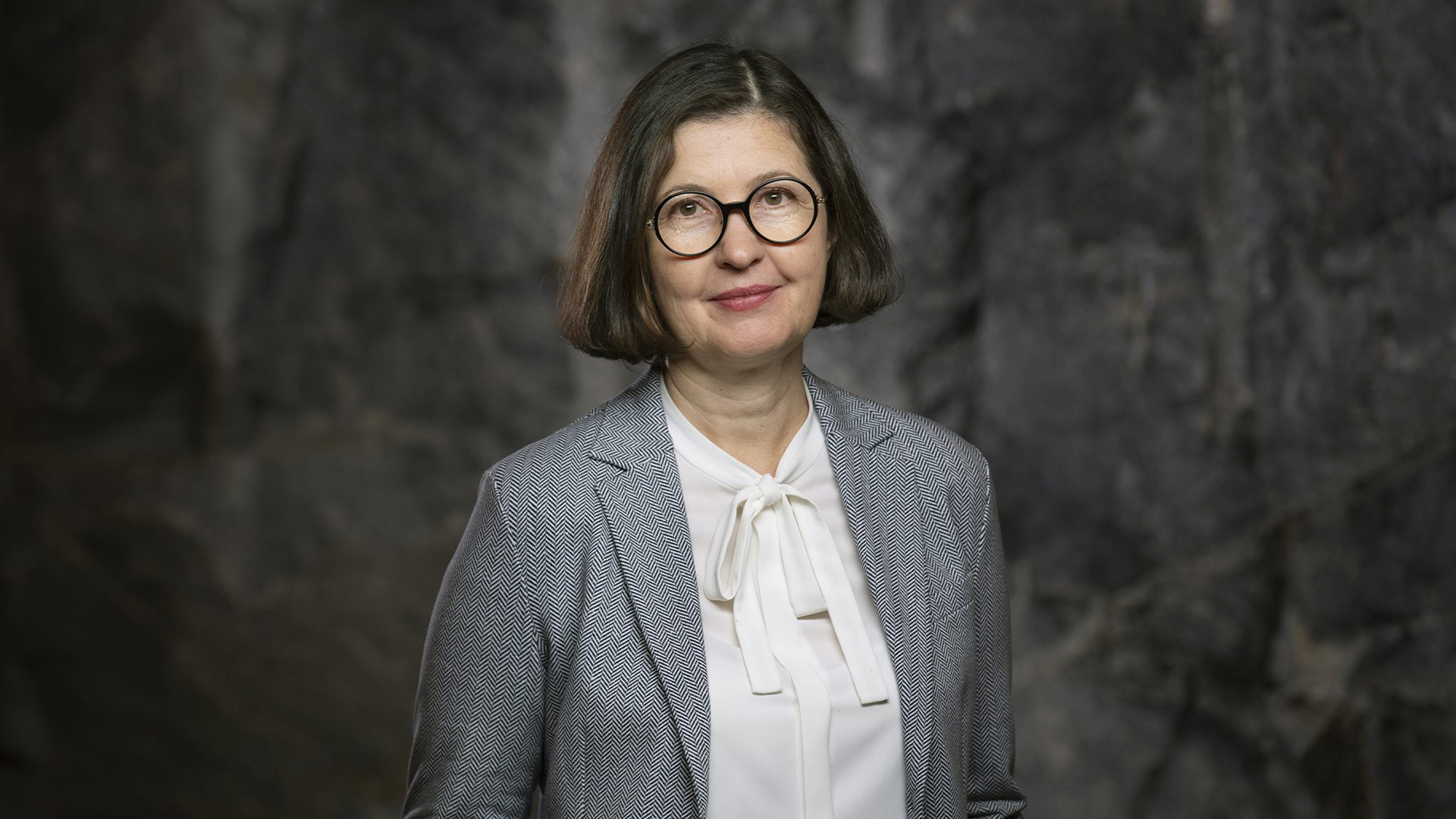 Porträttfoto av en kvinna i professionell kläder mot en grå bakgrund.