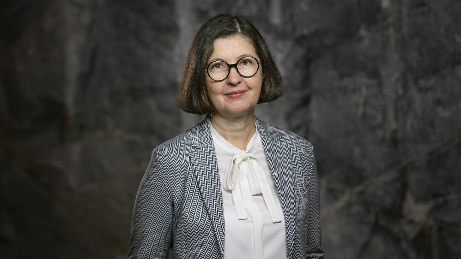 Porträttfoto av en kvinna i professionell kläder mot en grå bakgrund.