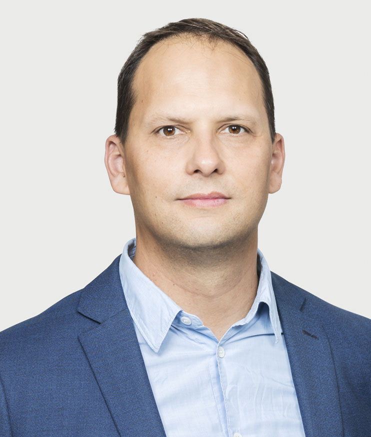 Porträtt av en man i blå kavaj och ljusblå skjorta mot neutral grå bakgrund