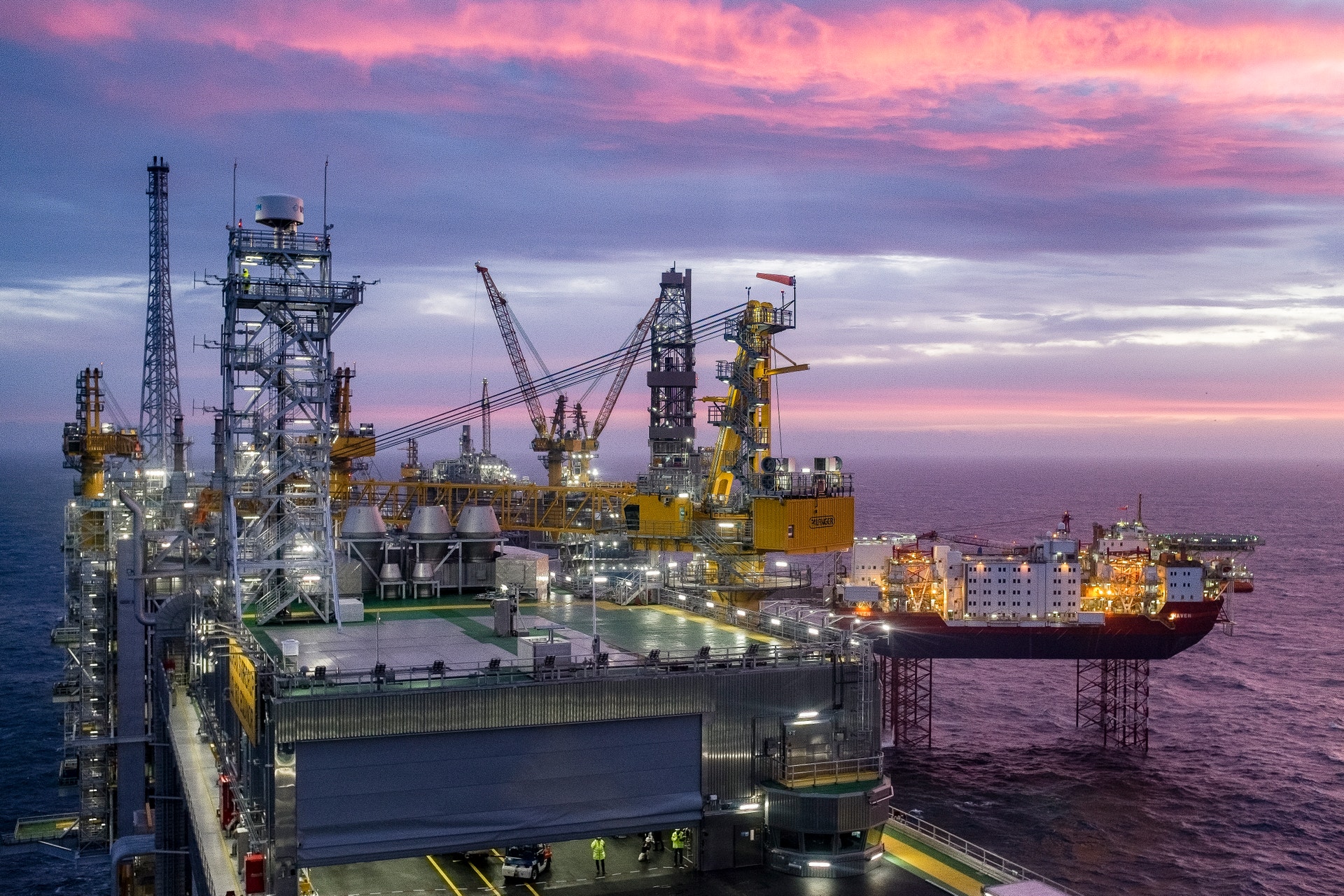 En oljeplattform till havs i skymning med en rosa himmel.