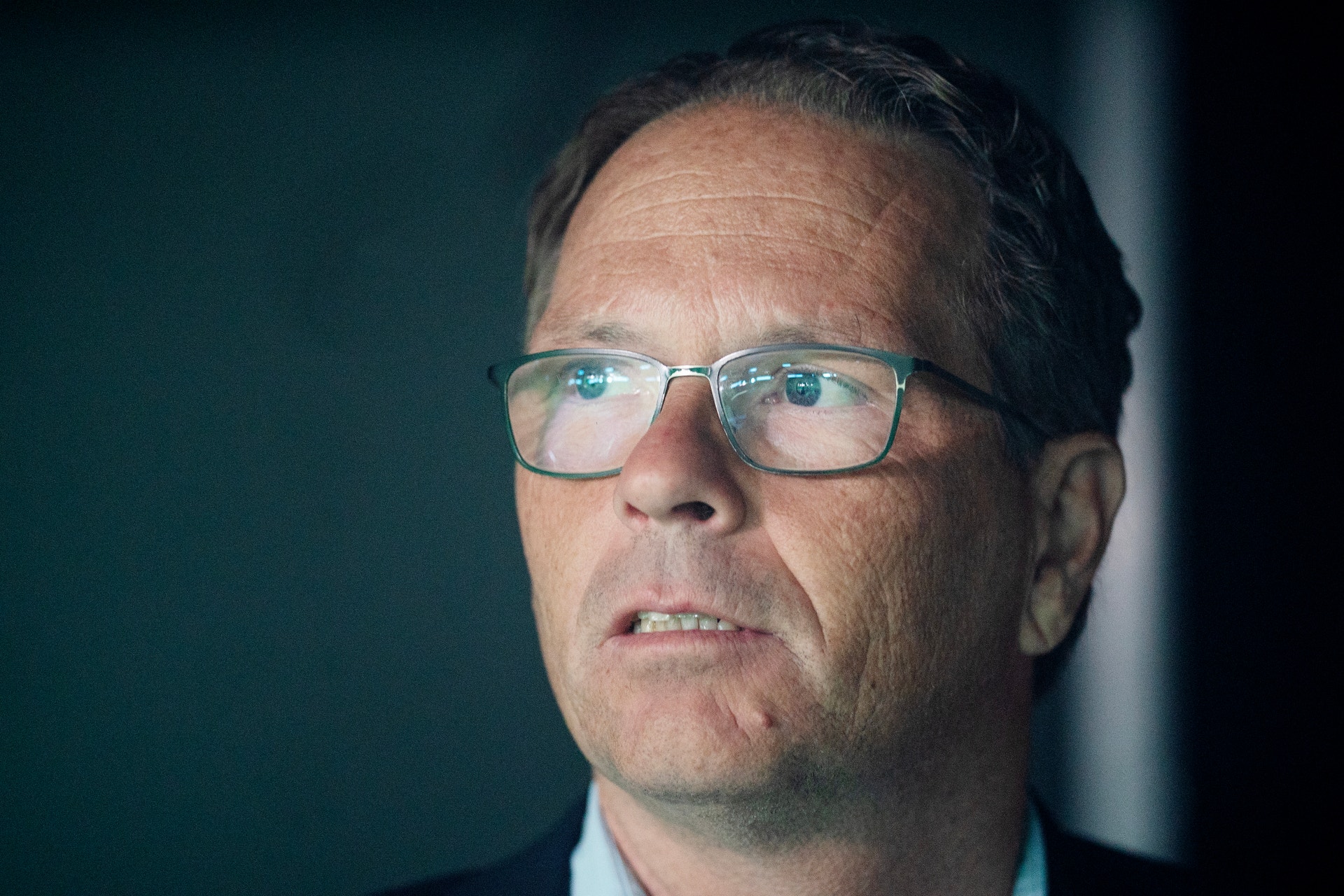 Porträtt av Inge Heydorn, man med glasögon mot mörk bakgrund.