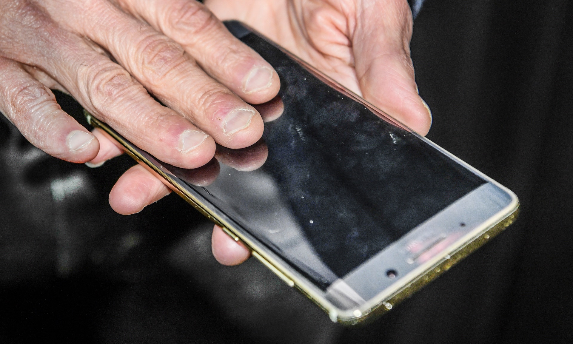 Två händer håller en smartphone med svart skärm och guldfärgad ram.
