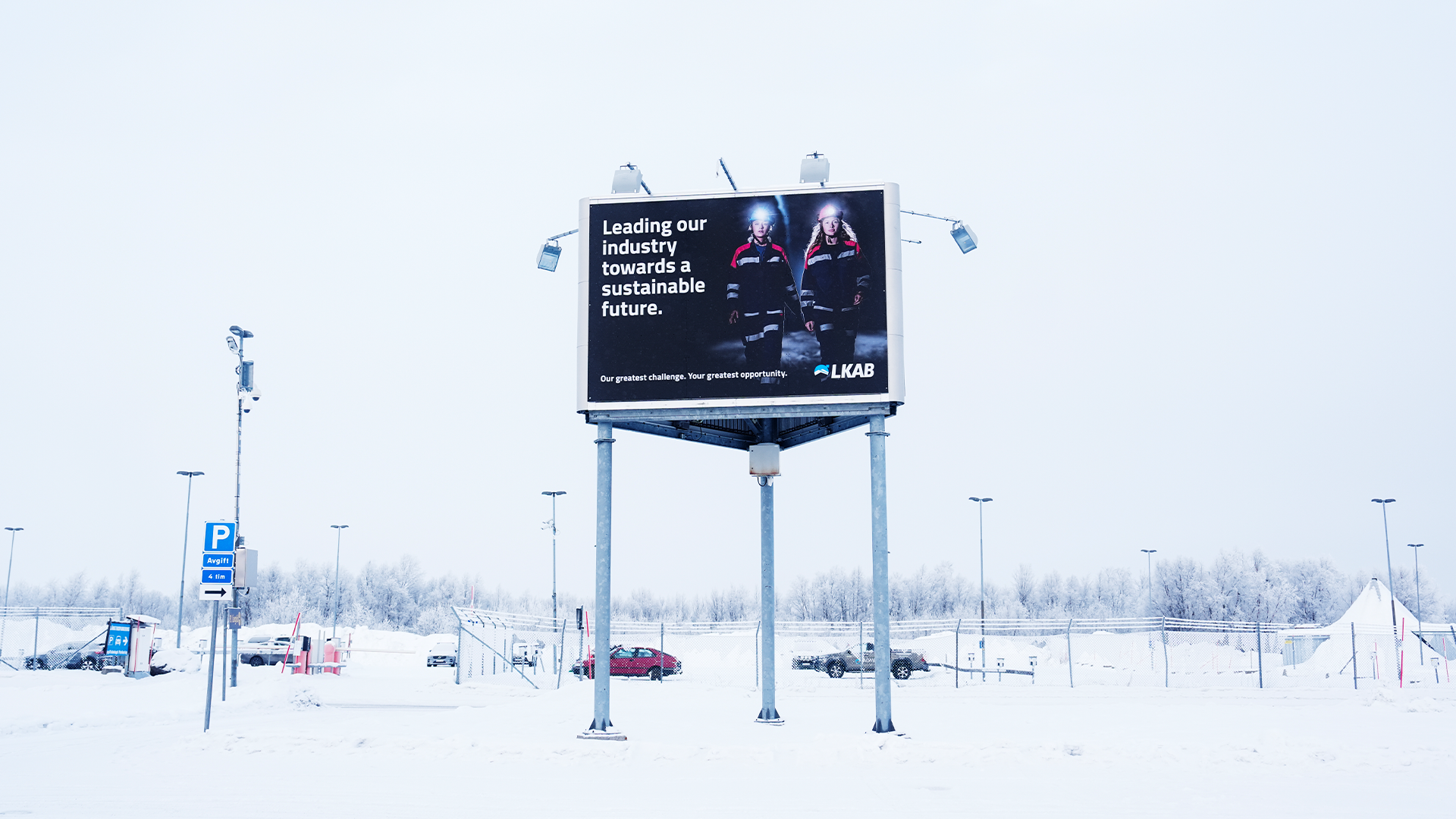 En stor reklamskyllt i ett snöigt industriområde med text om hållbar framtid.