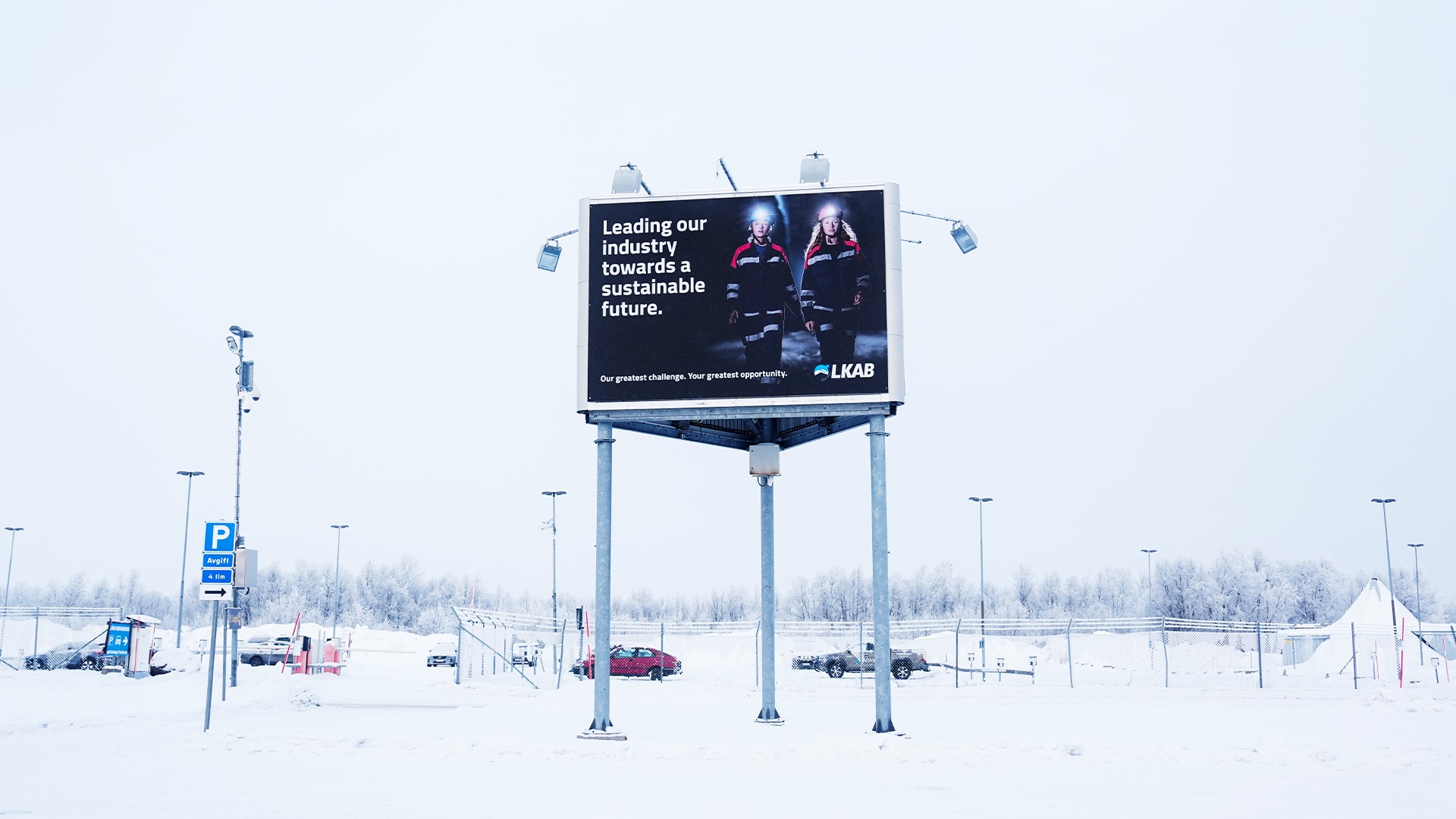 En stor reklamskyllt i ett snöigt industriområde med text om hållbar framtid.