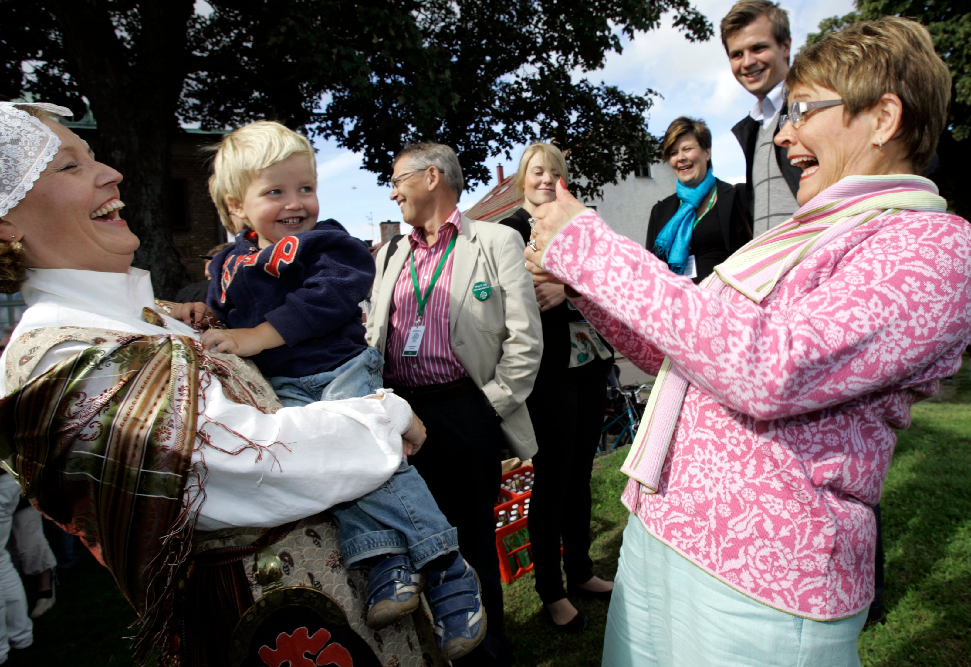 En grupp människor samlas utomhus under ett stort träd vid ett gemenskapsevenemang.