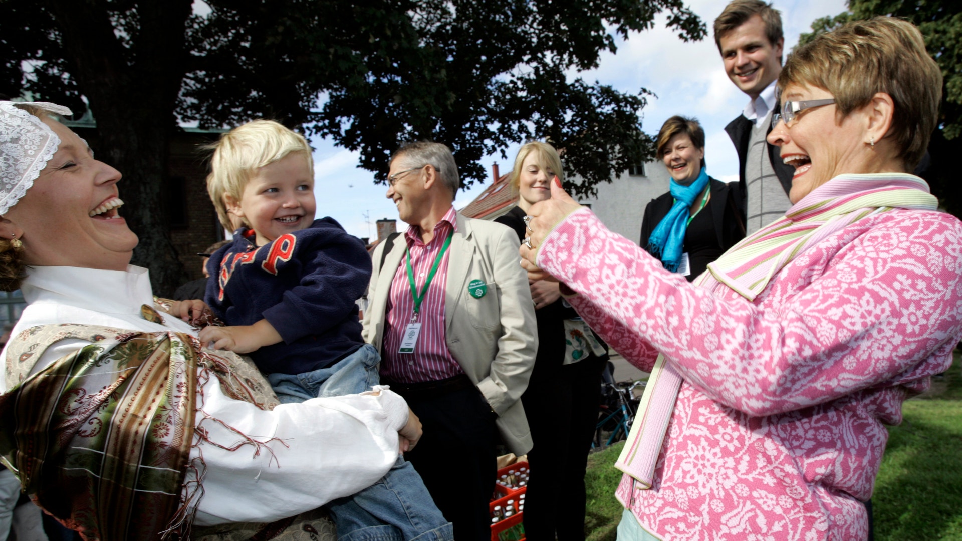 En grupp människor samlas utomhus under ett stort träd vid ett gemenskapsevenemang.