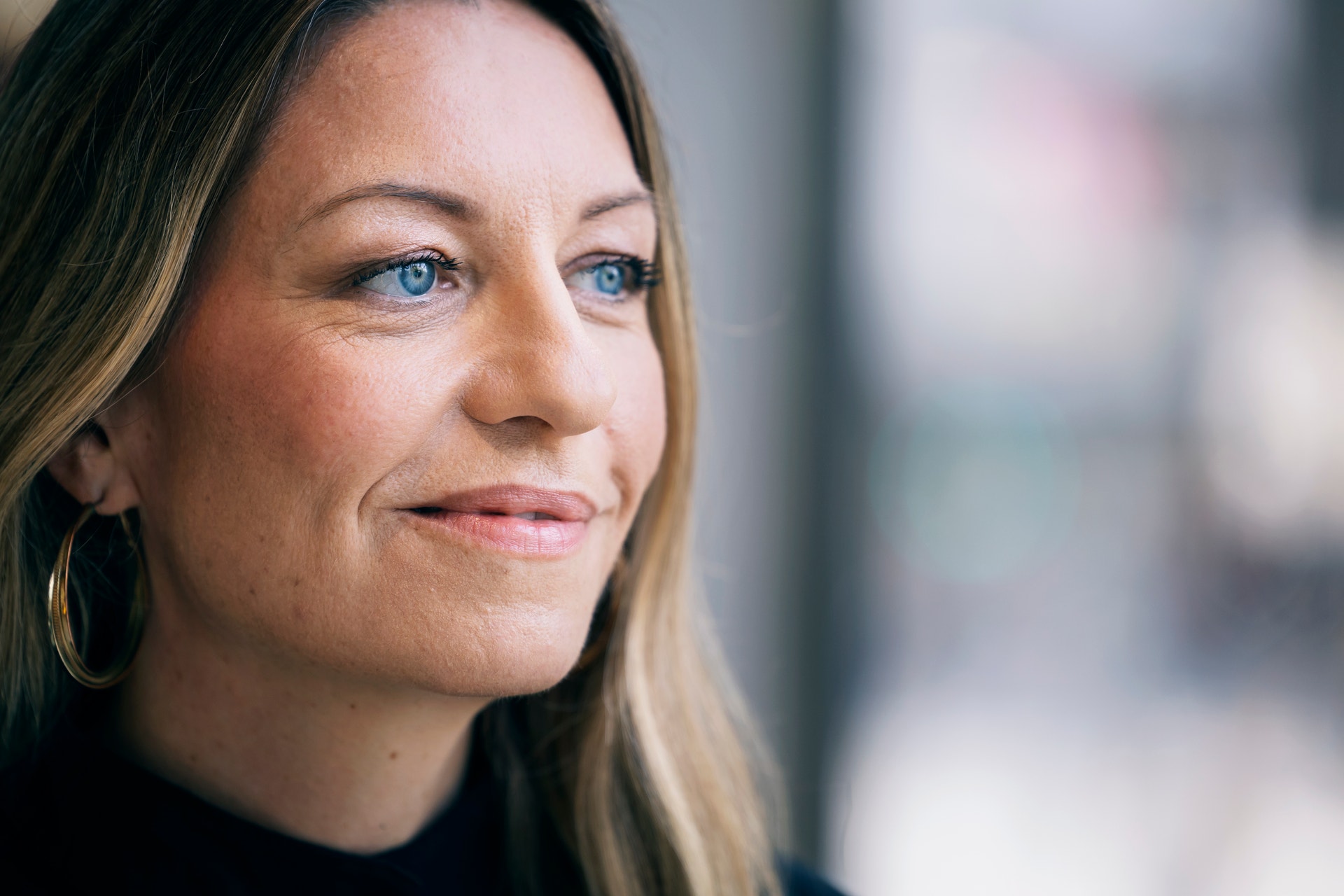 Porträtt av en kvinna med ljust hår och blå ögon som tittar mot kameran med ett lugnt leende.