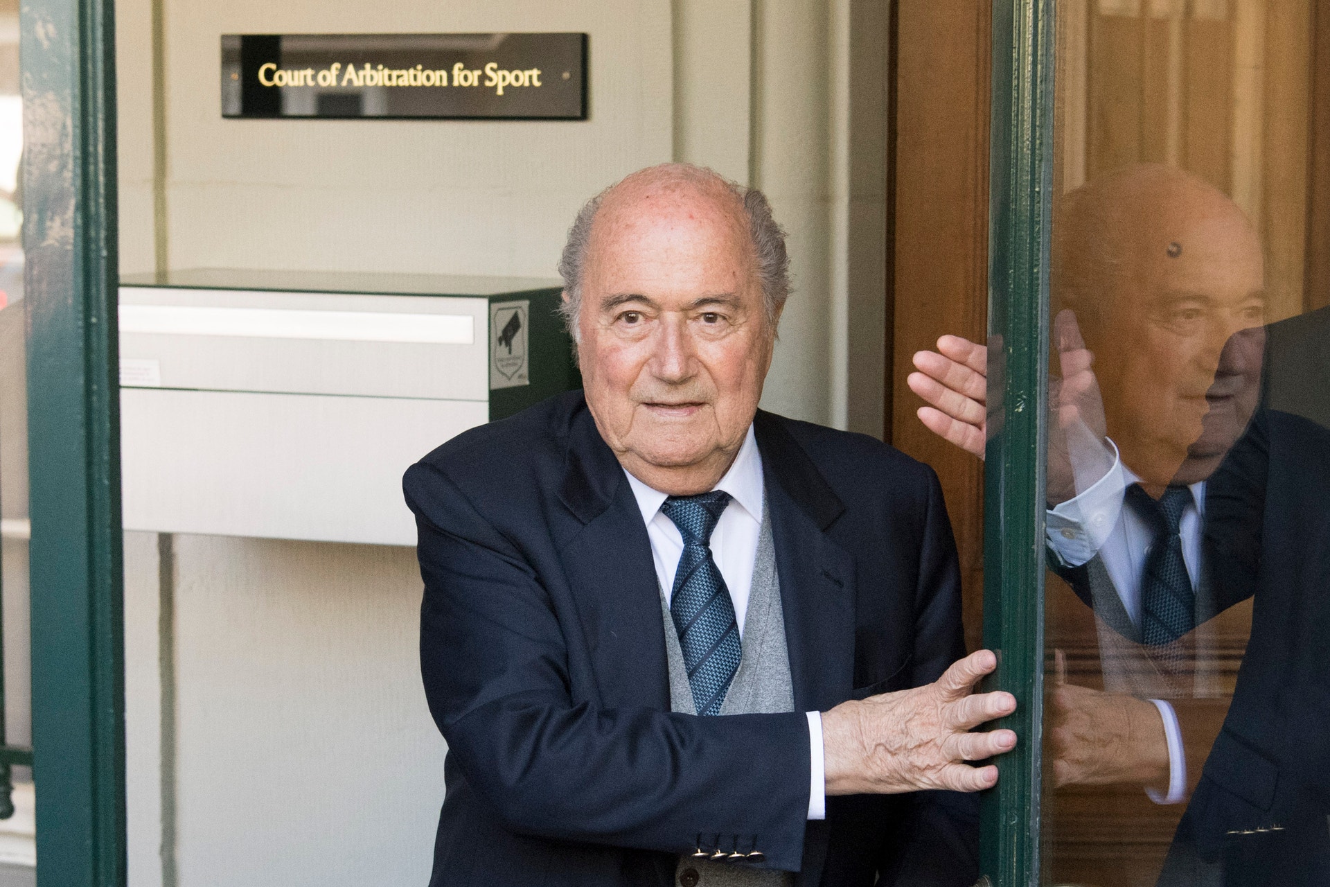 Äldre man i mörk kostym och blå slips vid dörren till Court of Arbitration for Sport.