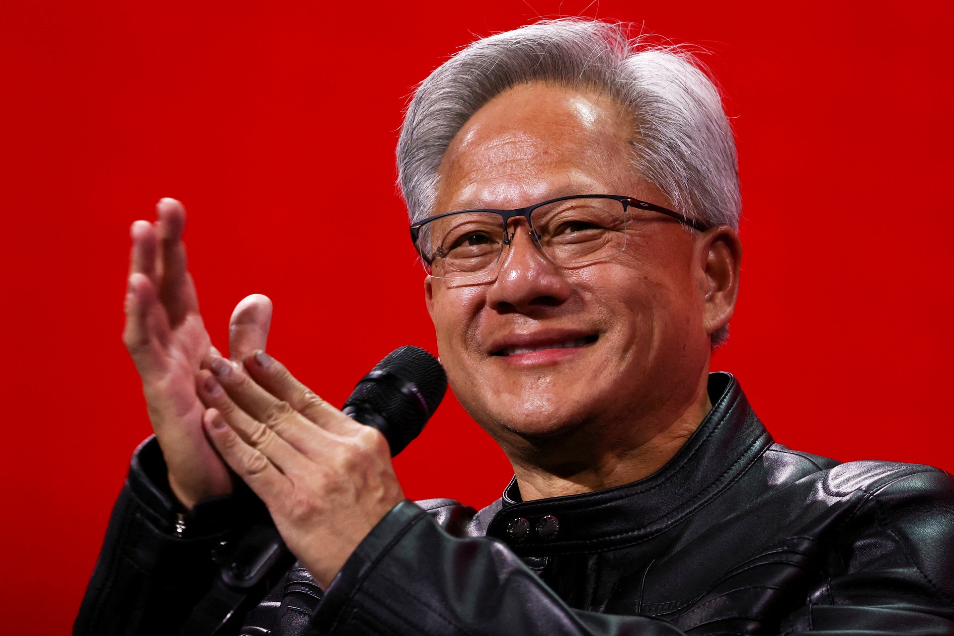 Nvidia:s vd Jensen Huang klappar händerna och ler till publiken när han står på en röd scen med en mikrofon i handen. 