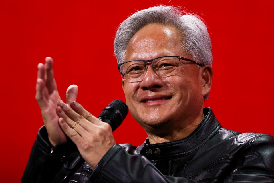 Nvidia:s vd Jensen Huang klappar händerna och ler till publiken när han står på en röd scen med en mikrofon i handen.