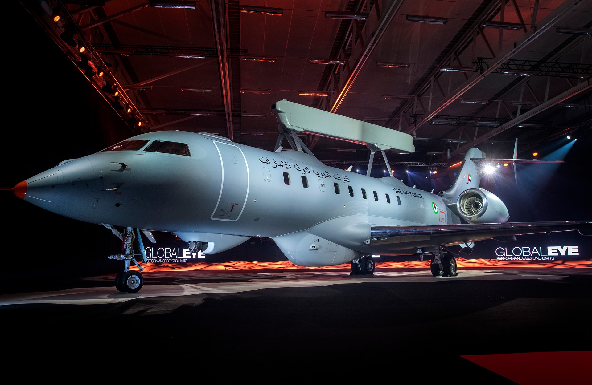 Ett modernt vitt passagerarflygplan står i en hangar under röd och blå belysning.