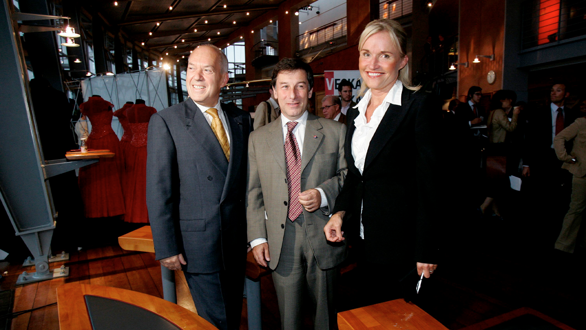 Tre personer i affärskläder på ett formellt event i en elegant inomhusmiljö.