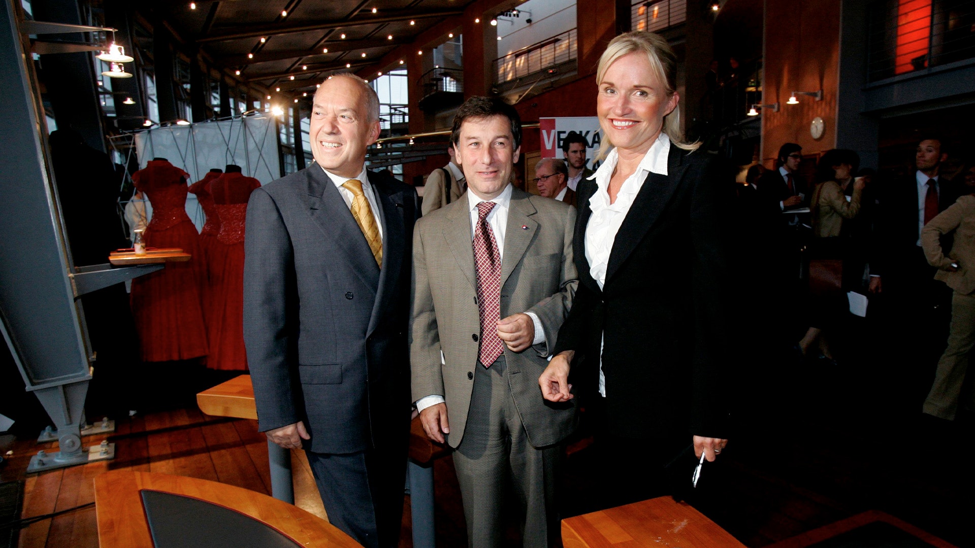 Tre personer i affärskläder på ett formellt event i en elegant inomhusmiljö.