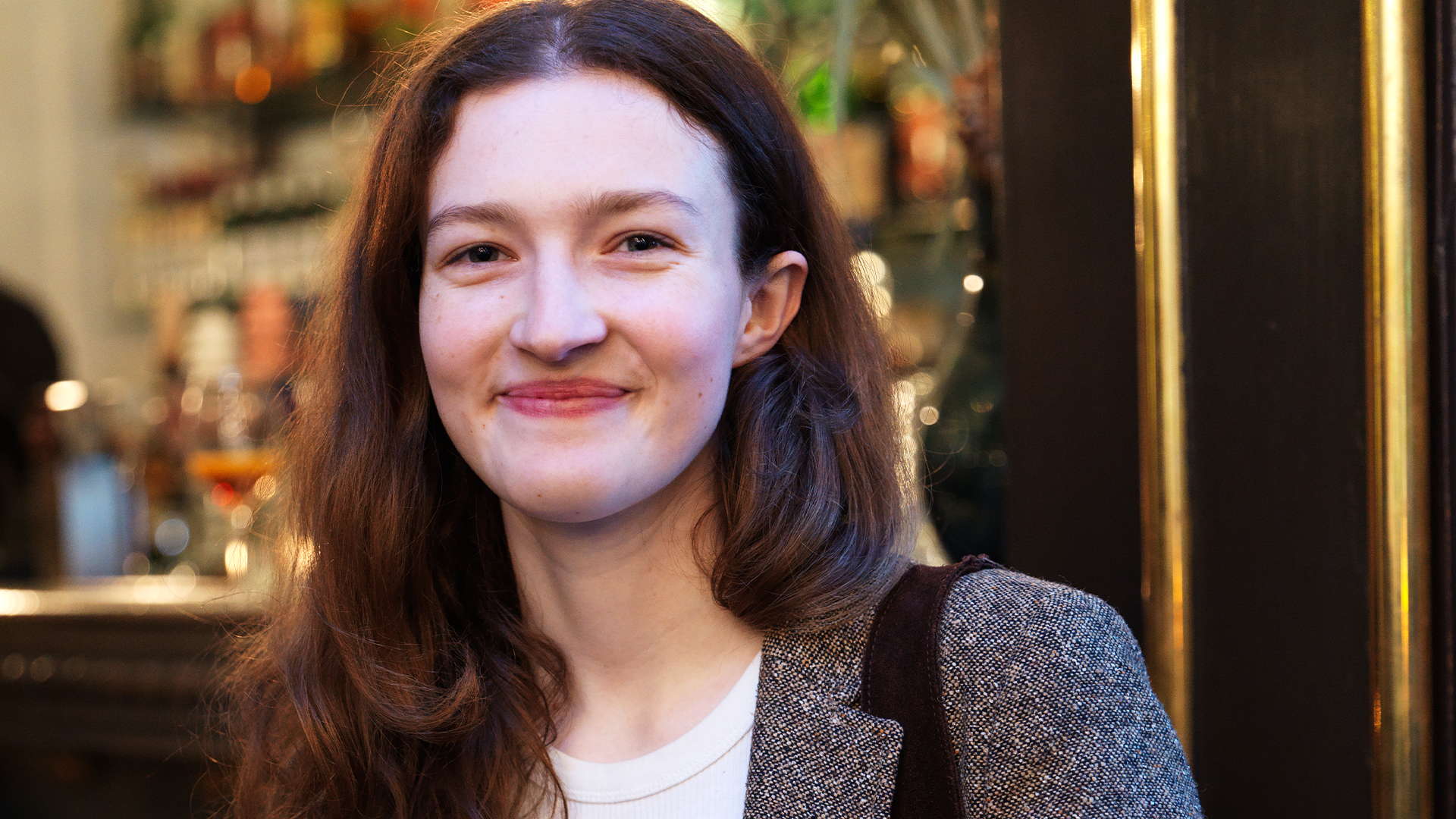 Porträtt av en ung kvinna med långt mörkt hår som ler mot kameran