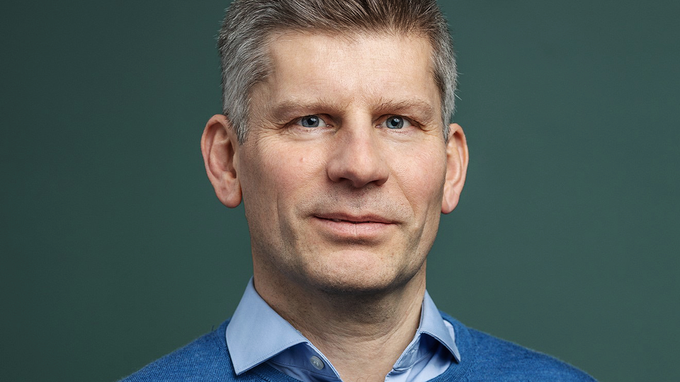 Porträttfoto av en man i blå skjorta mot grön bakgrund