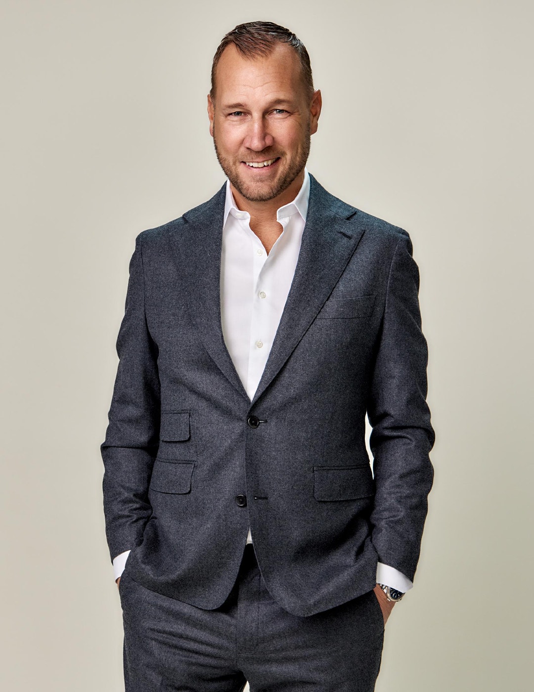 Porträttfoto av en man i mörkgrå kostym och vit skjorta mot en ljus bakgrund.