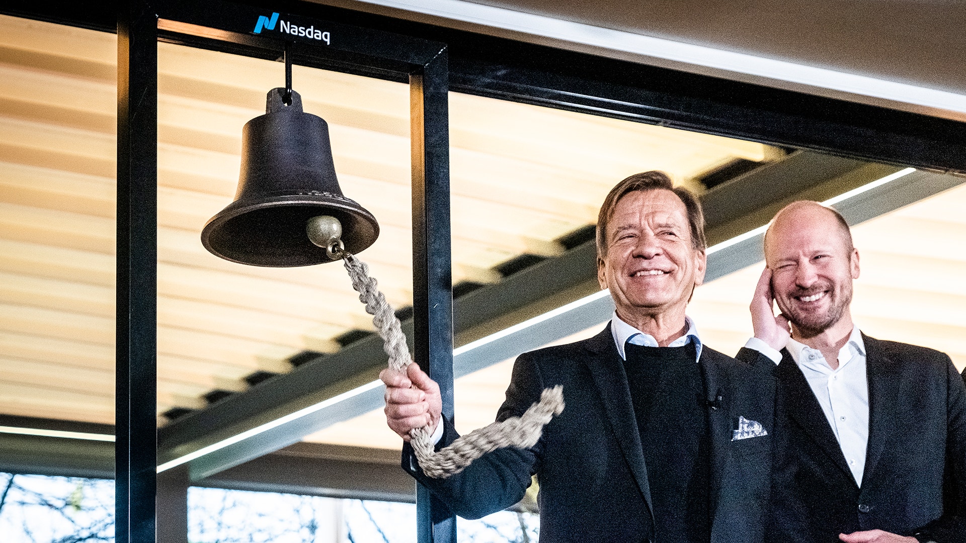 Två män i kostym ringer en stor klocka vid Nasdaq-börsen.