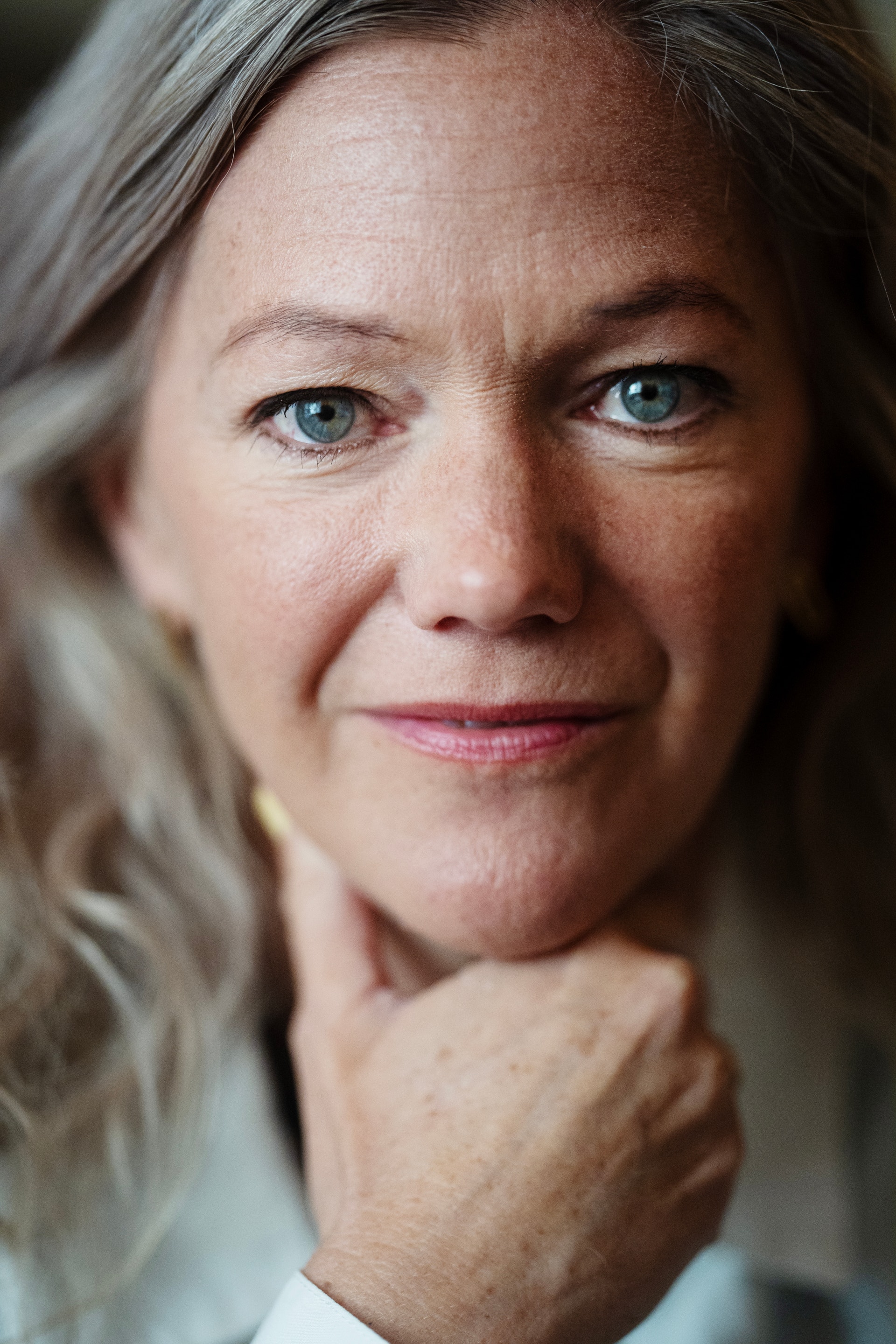Porträtt av en kvinna med gråsprängt hår som tittar in i kameran.