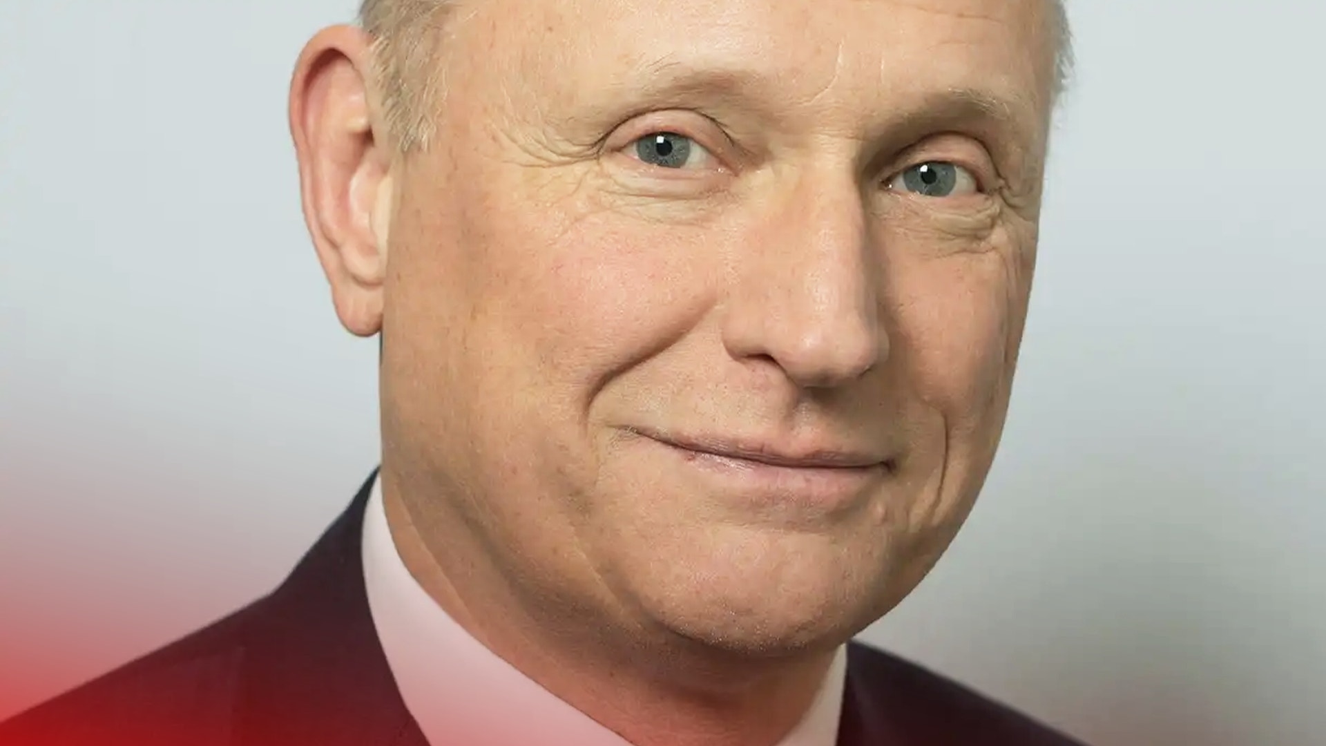 Porträttfoto av en man i röd skjorta och rosa slips som ler mot kameran.