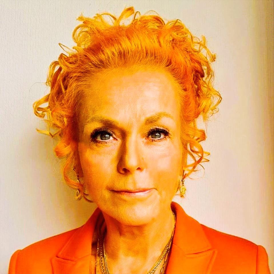Porträtt av en kvinna med lockigt orangegult hår, iklädd orange jacka.