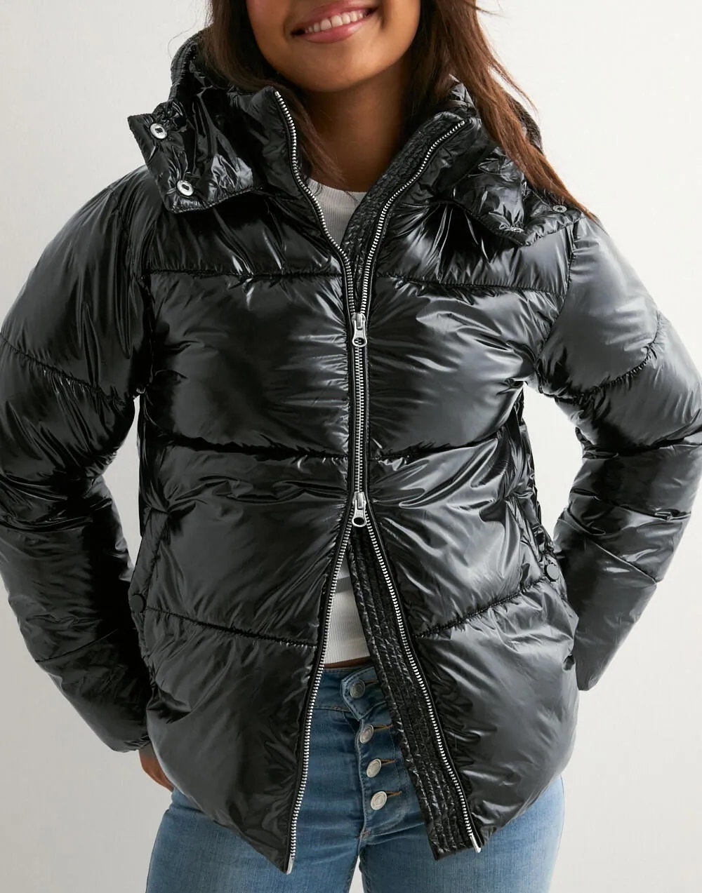 En leende kvinna bär en glansig svart täckjacka med huva och jeans.