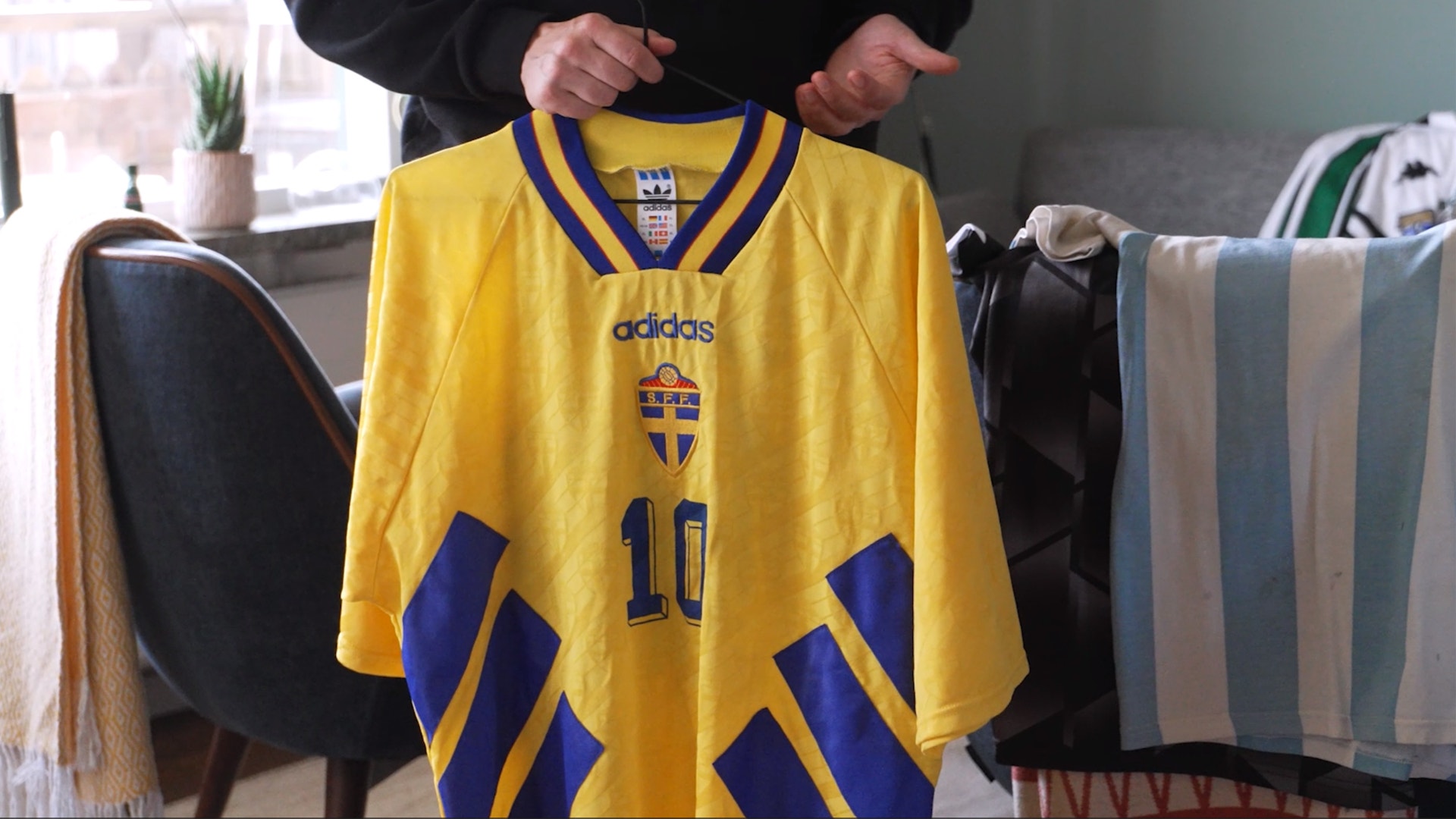 En gul baskettröja med blå detaljer och det svenska riksvapnet, hållen upp av en person.