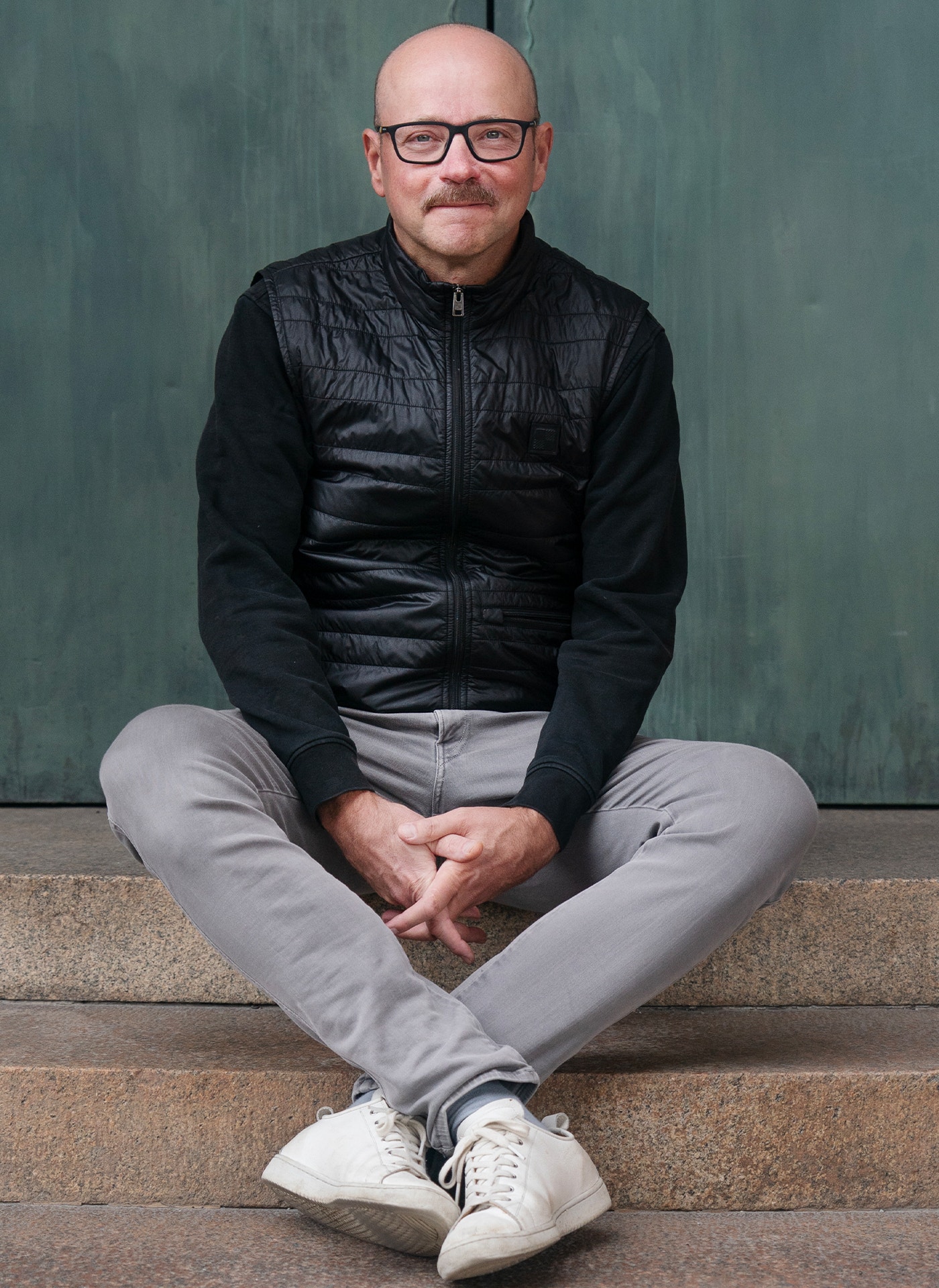 Pål Ahlsén sitter på en trappa framför en grön kopparport. Han har benen i kors. Han ler.