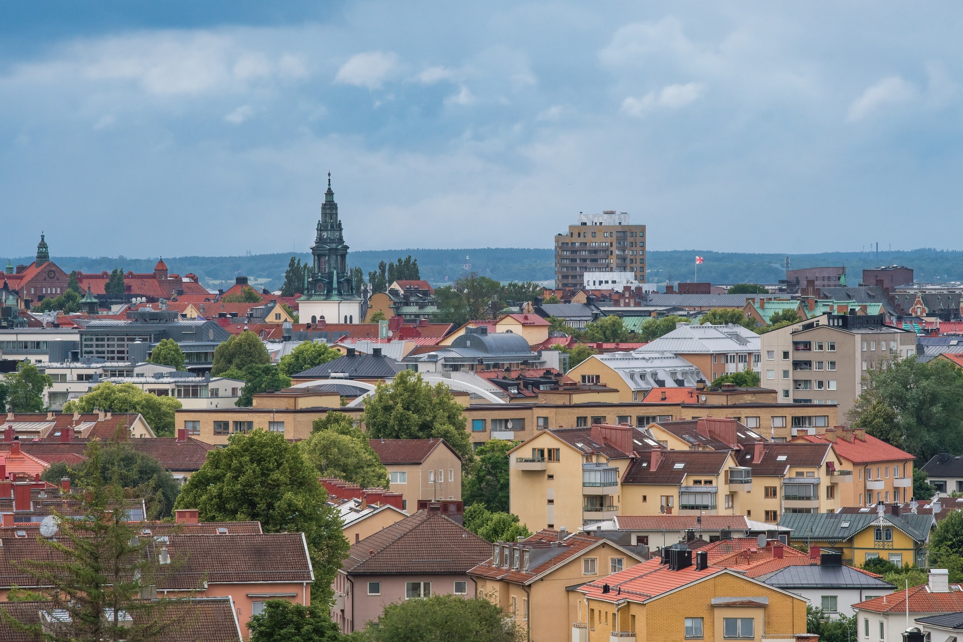 Luftfoto över en europeisk stad med färgglada bostadshus, kyrktorn och träd under blå himmel med moln.
