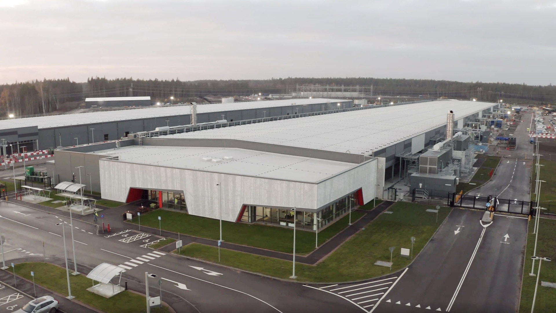 Flygbild över ett stort datacenter med långa vita industribyggnader, omgivet av skog.