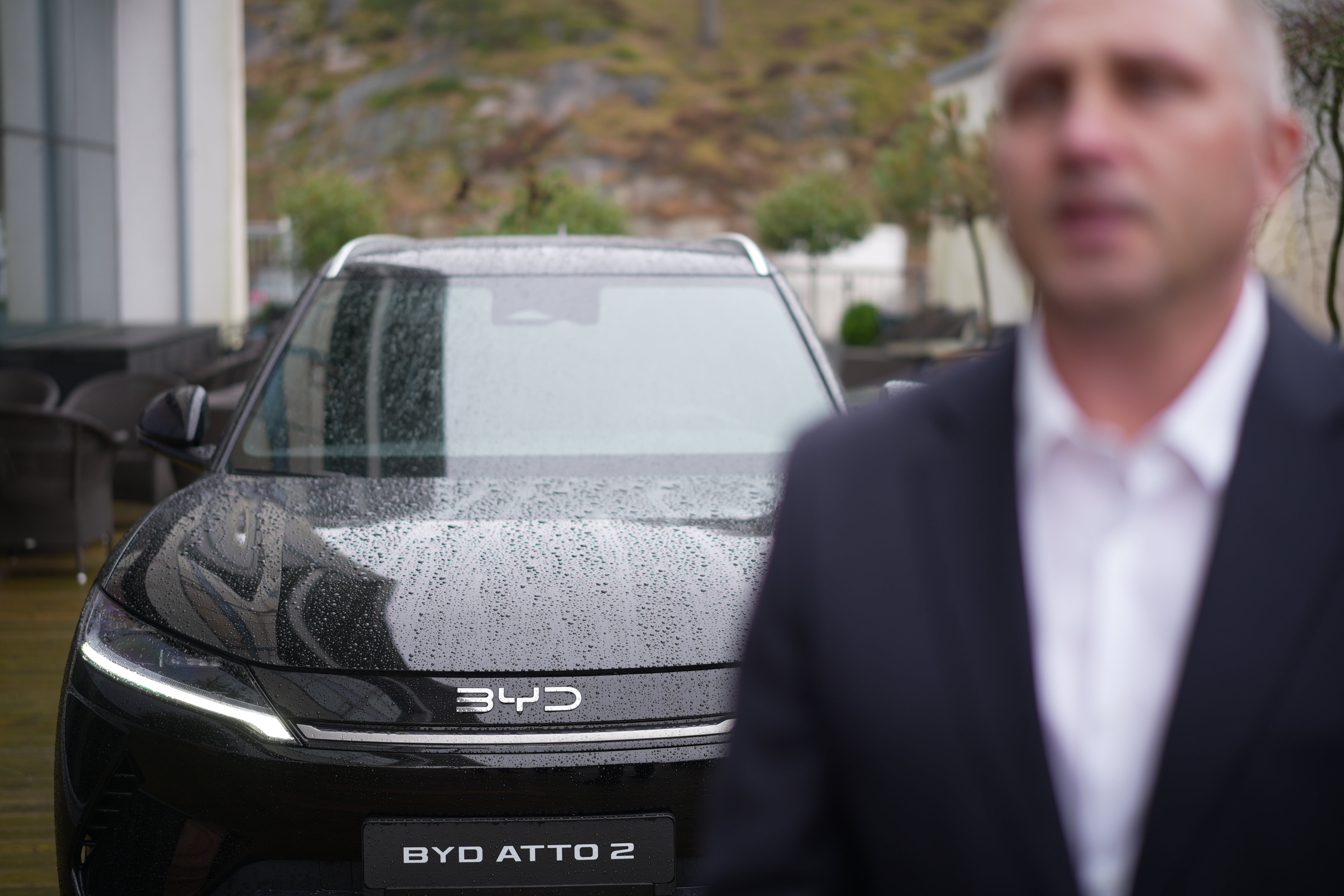 En man i kostym står framför en våt BYD Atto 2 elbil