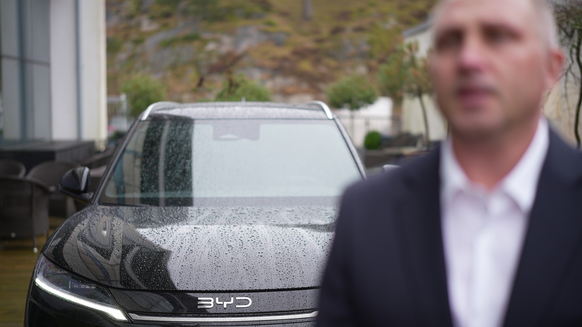 En man i kostym står framför en våt BYD Atto 2 elbil