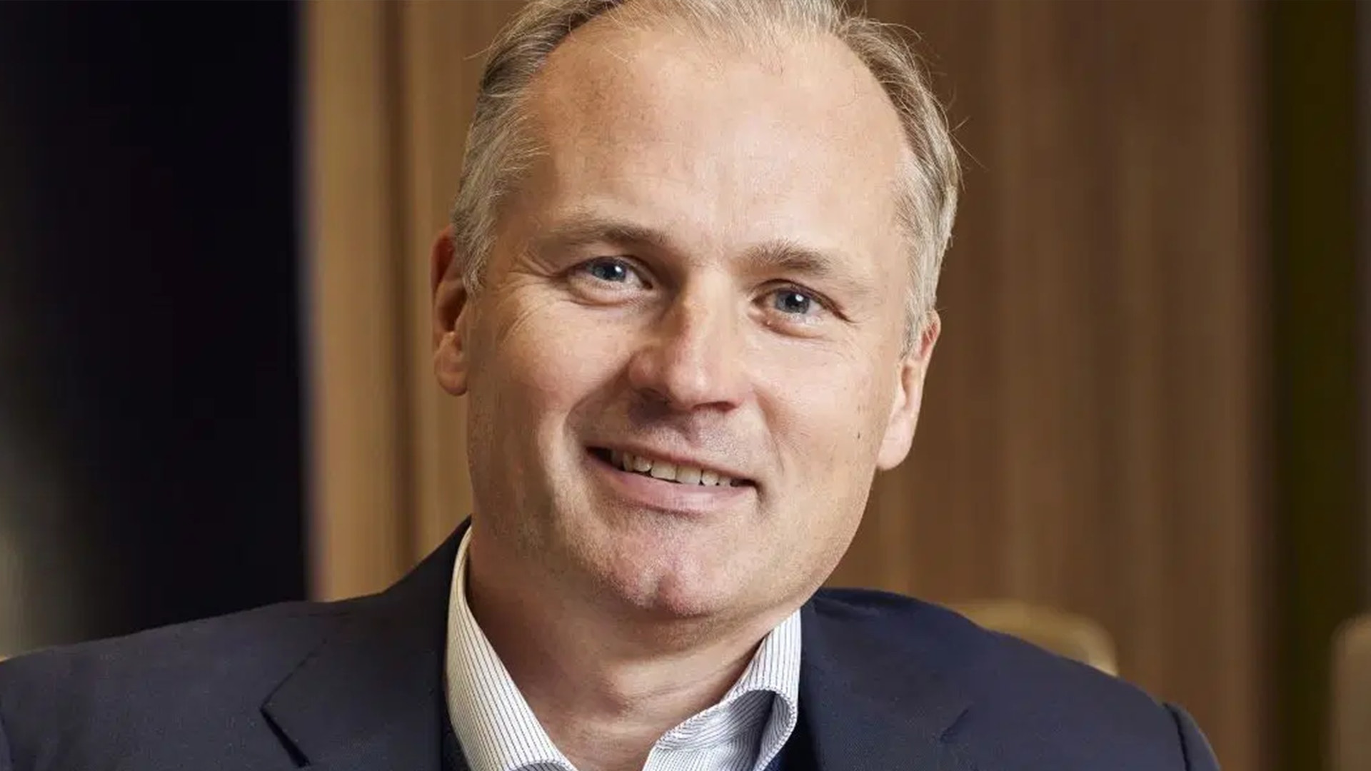 Porträttfoto av Roger Hedberg, en man i mörkblå kavaj och vit skjorta som ler mot kameran.