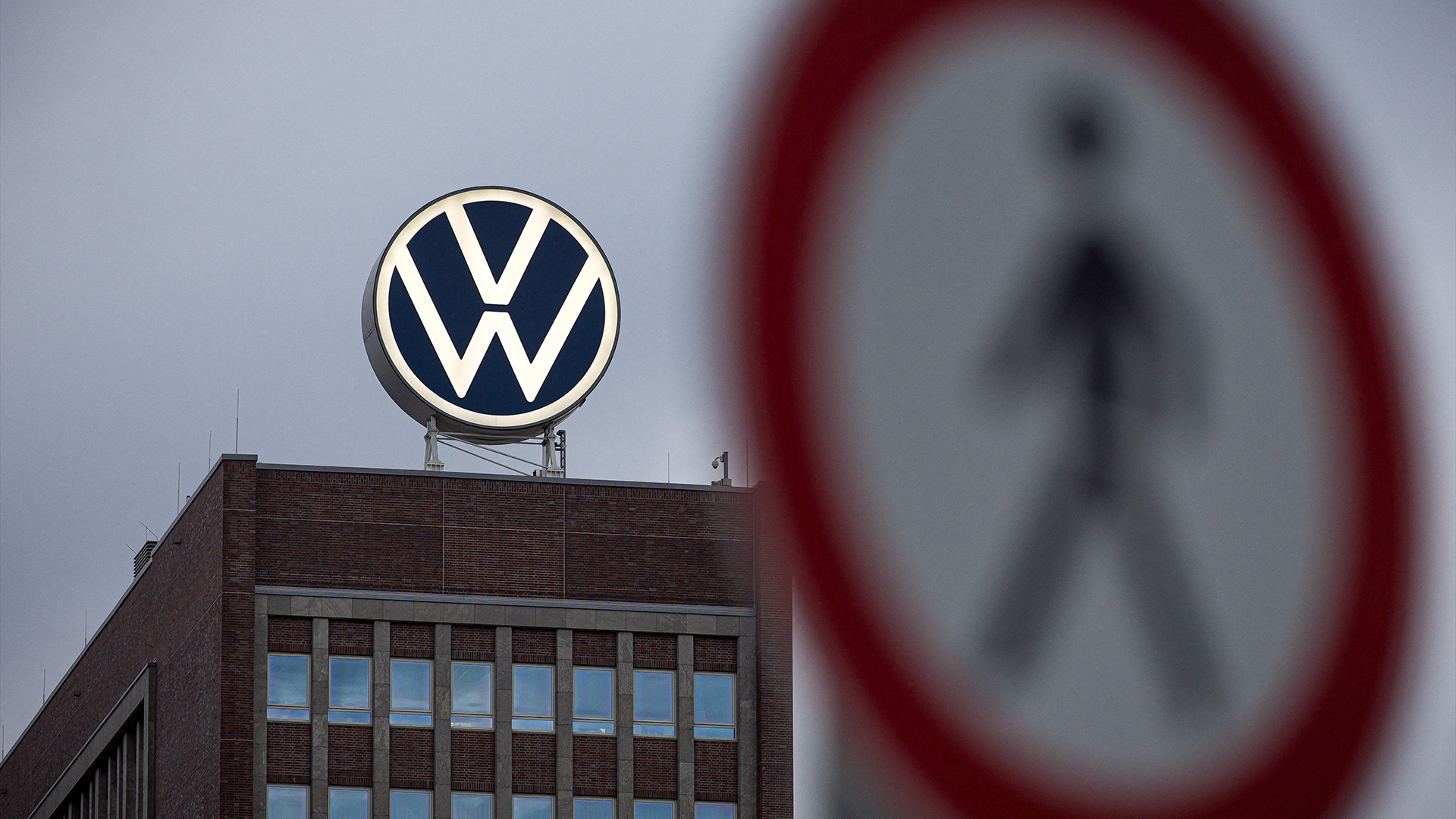 Volkswagens logotyp på en byggnad med en förbjuden passage-skylt suddig i förgrunden.