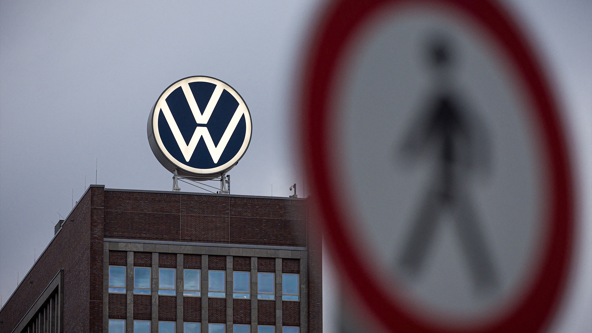 Volkswagens logotyp på en byggnad med en förbjuden passage-skylt suddig i förgrunden.