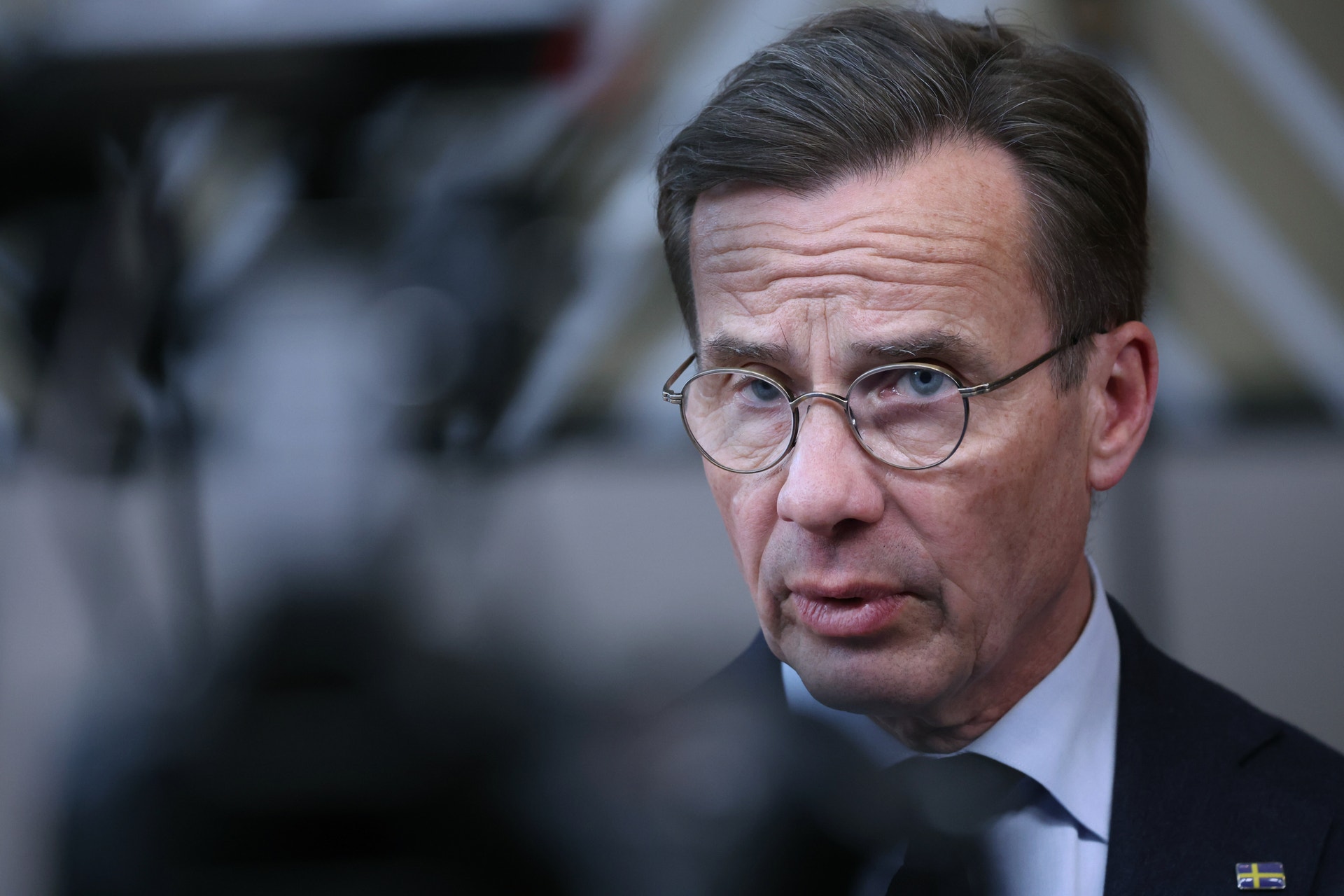 Ulf Kristersson, med glasögon och mörk kostym, blir intervjuad och tittar allvarligt framåt.