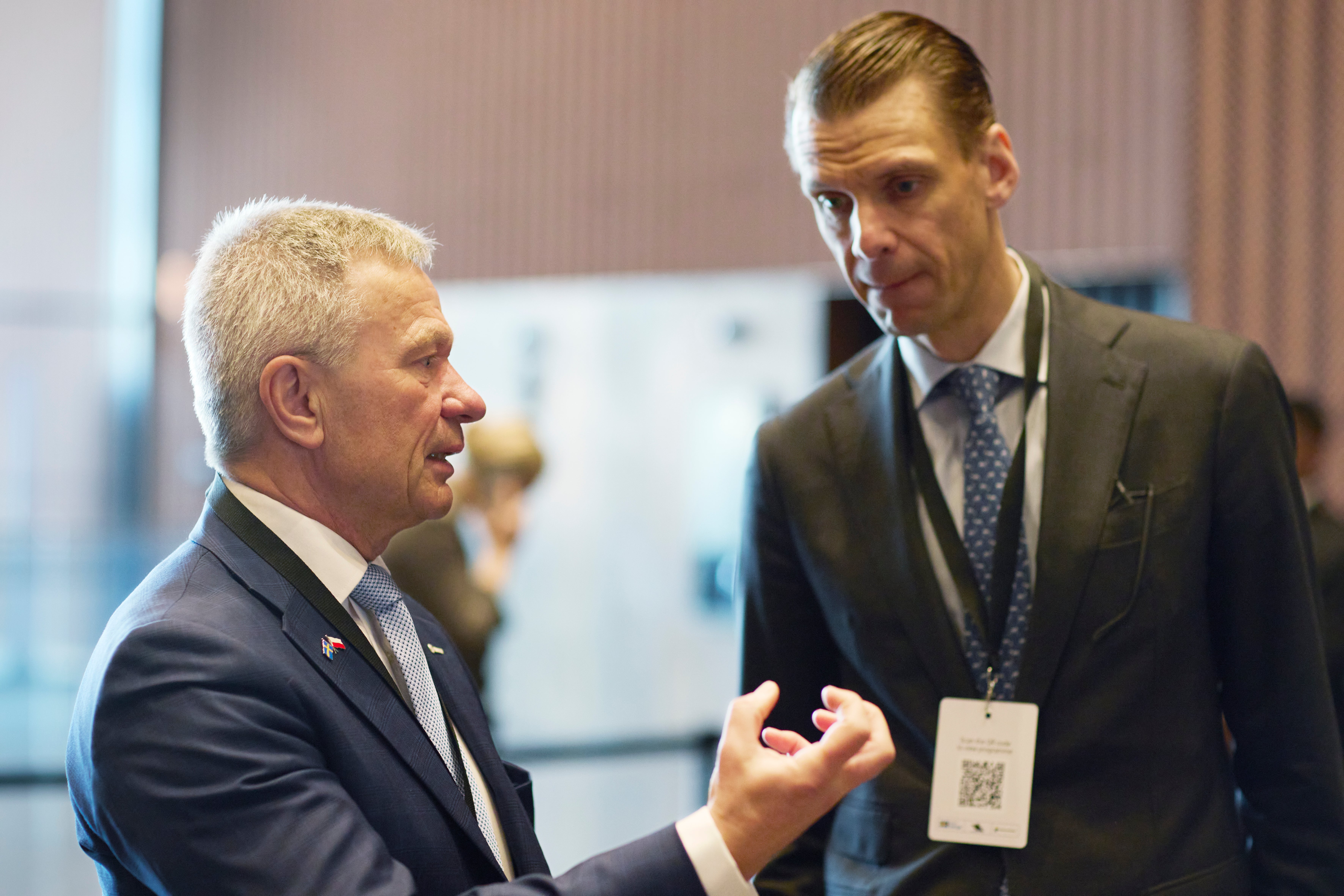 Två män i kostym diskuterar vid ett möte eller event.