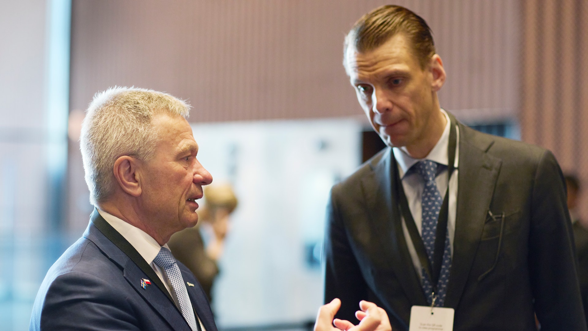 Två män i kostym diskuterar vid ett möte eller event.