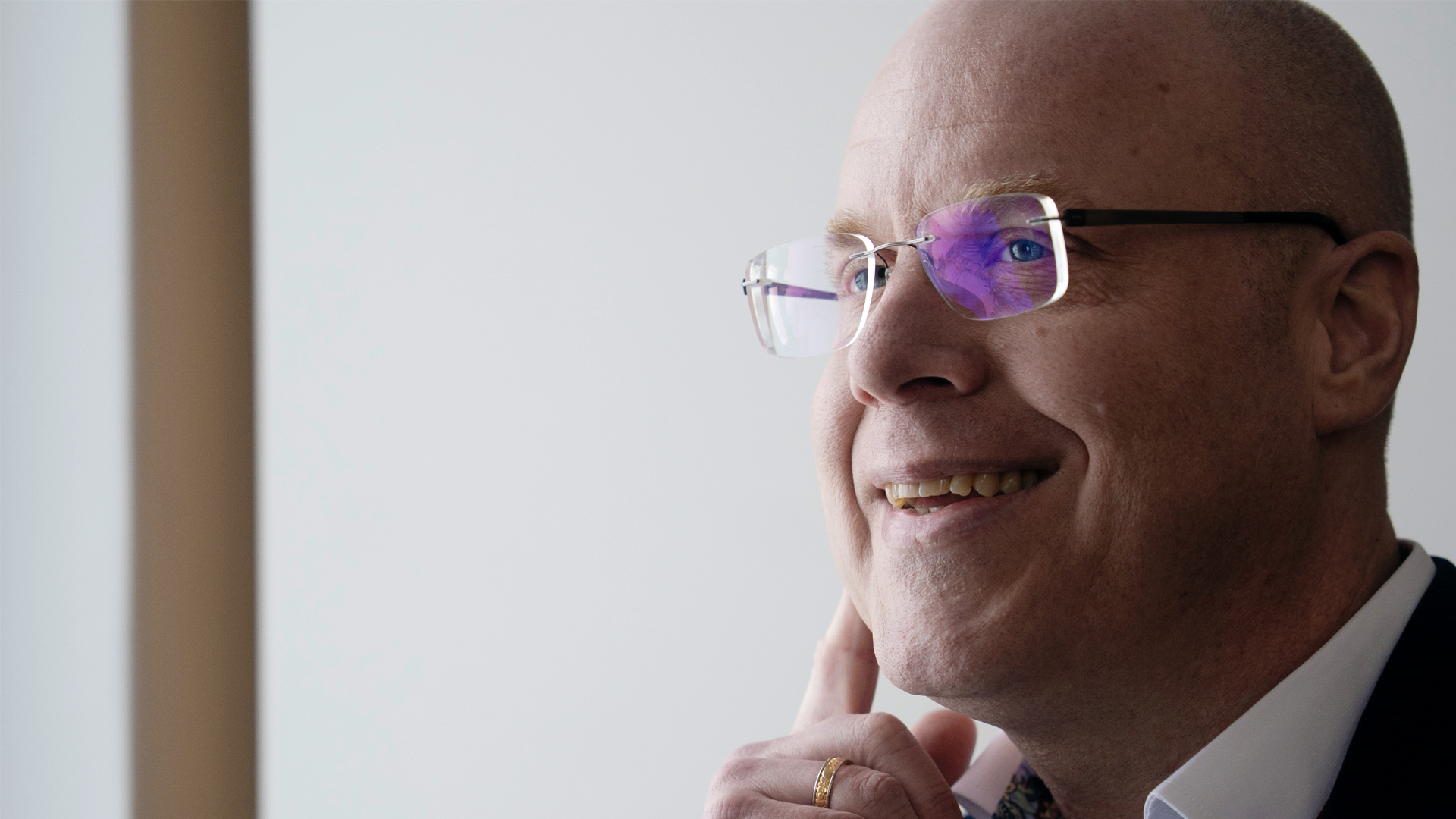 Porträttfoto av en man med glasögon och svart kavaj mot en ljus bakgrund. Mannen ler och tittar åt sidan.