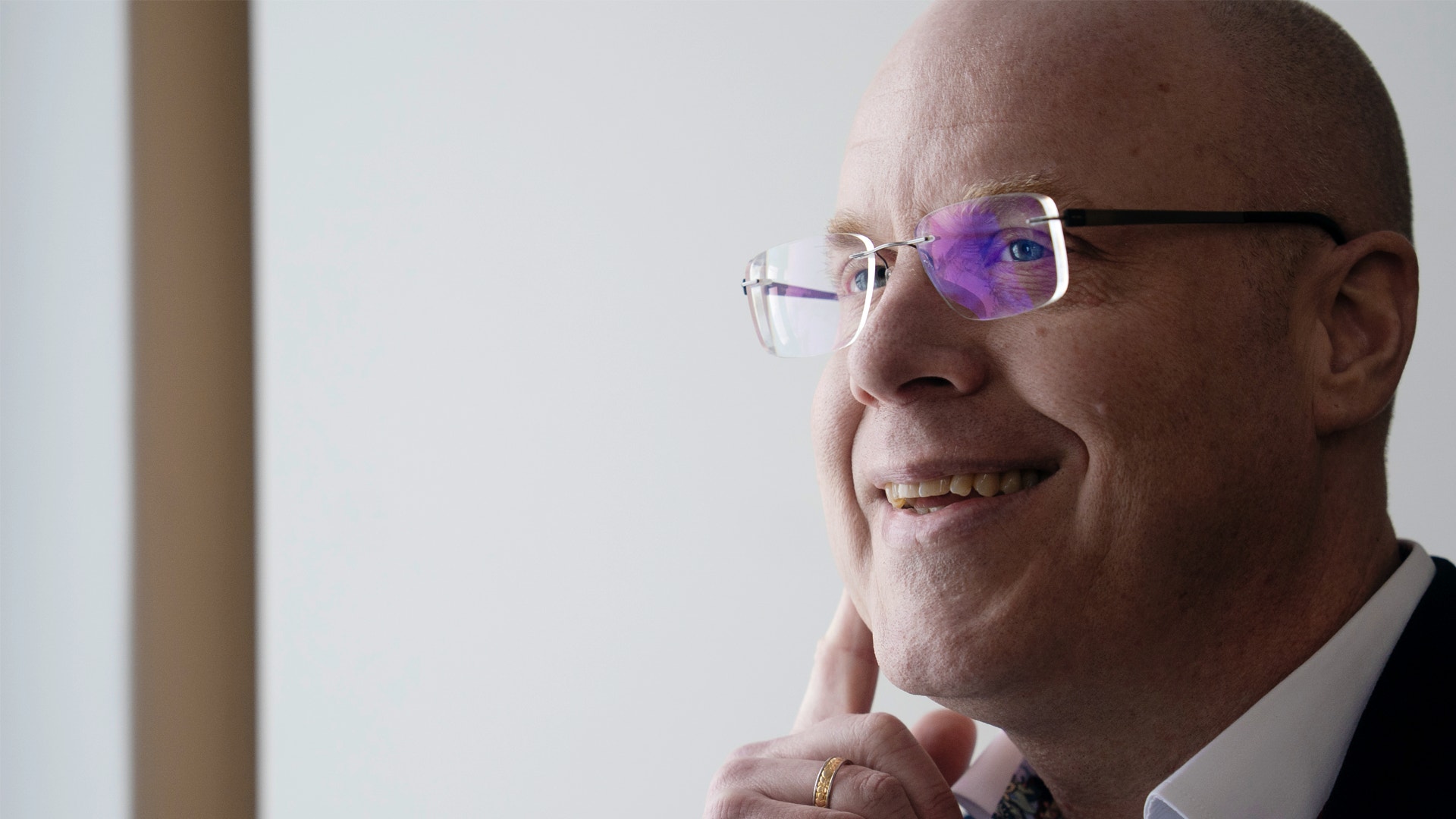 Porträttfoto av en man med glasögon och svart kavaj mot en ljus bakgrund. Mannen ler och tittar åt sidan.