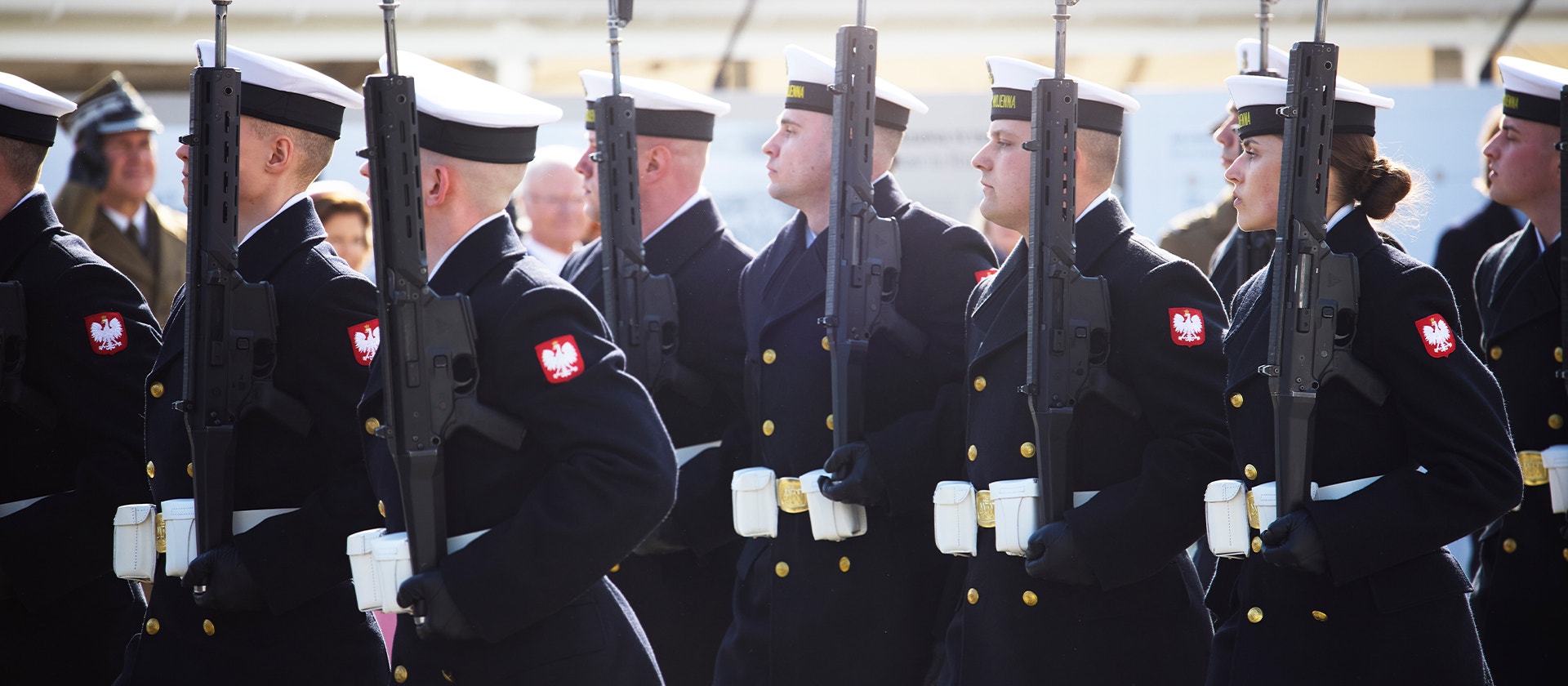 Polsk militär i formell ceremoni med soldater i mörkblå uniformer som håller gevär i formation.
