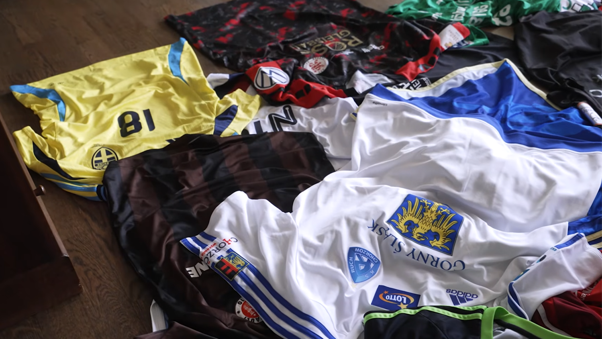 En samling fotbollströjor i olika färger utlagda på ett trägolv.